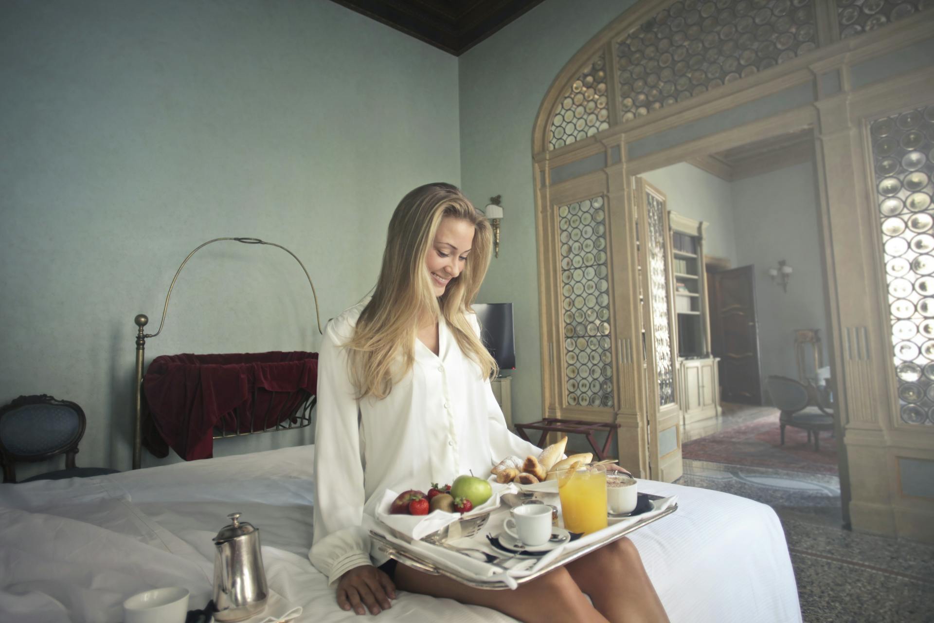 Une femme joyeuse avec un petit déjeuner sur un plateau dans une chambre d'hôtel | Source : Pexels