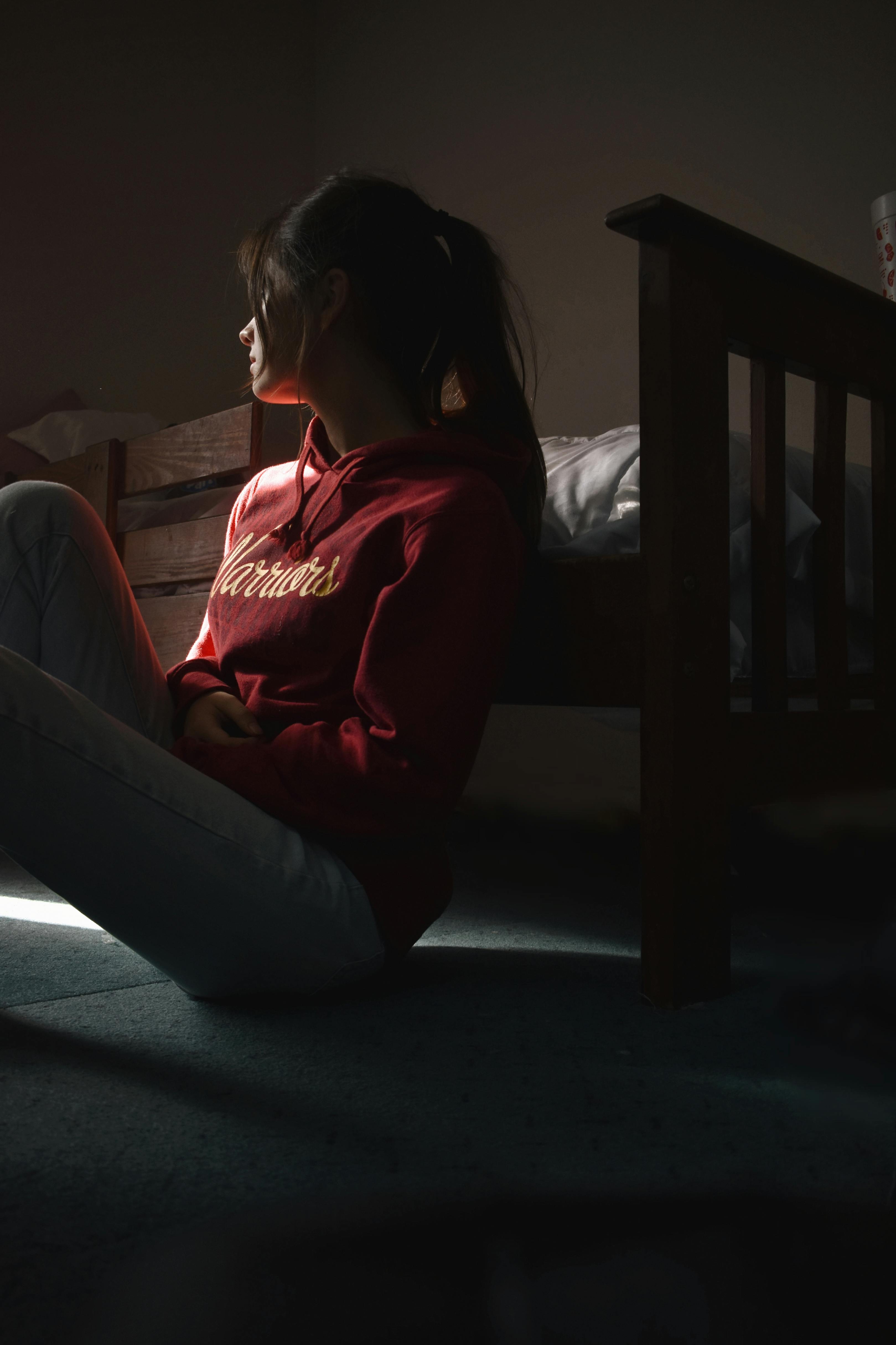 Silhouette partielle d'une femme triste assise sur le sol à côté de son lit | Source : Pexels