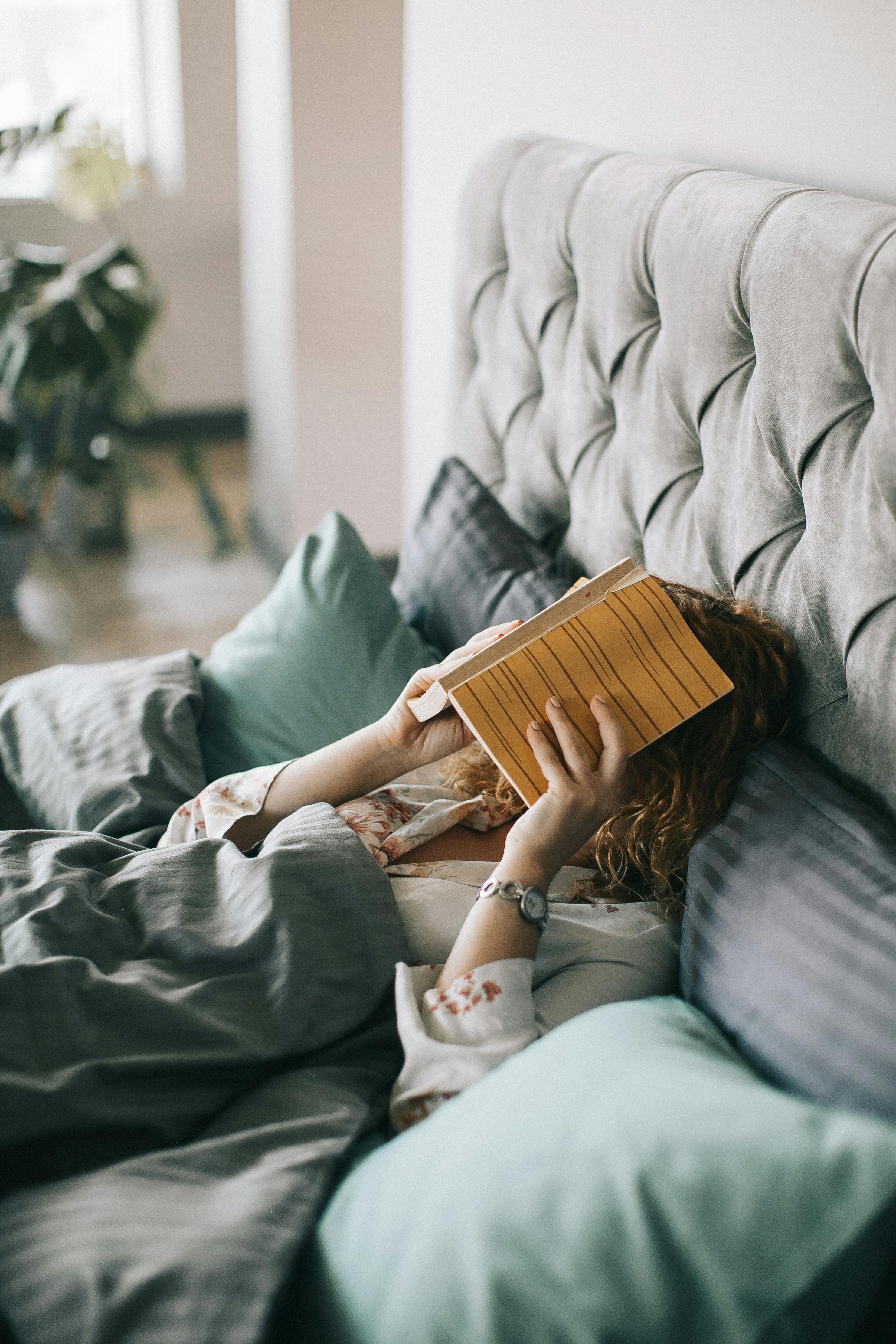 Une femme allongée dans son lit avec un livre couvrant son visage | Source : Pexels