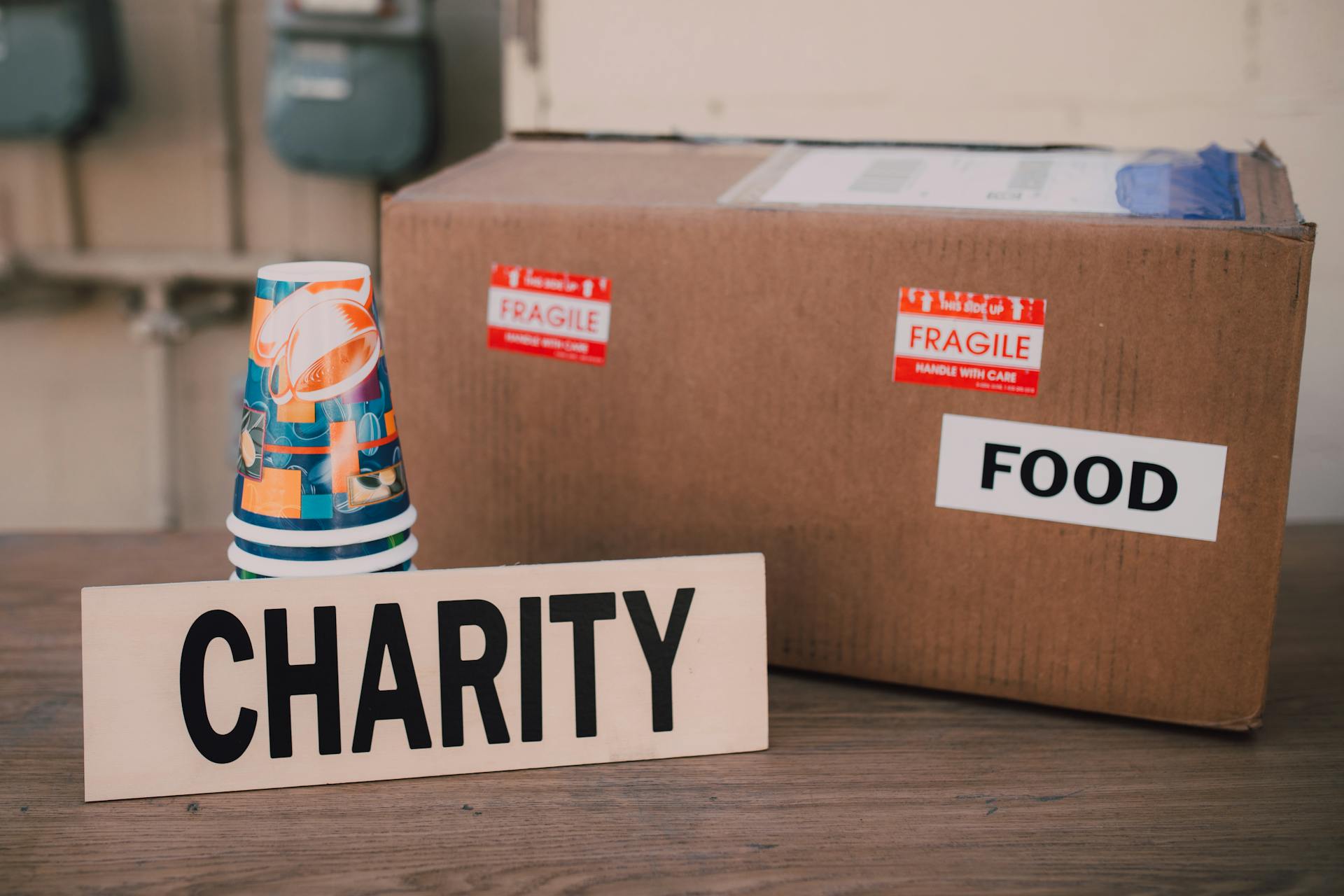 Une boîte en carton et une pile de gobelets en papier à côté d'un panneau de charité | Source : Pexels