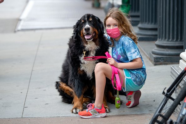 Une jeune fille portant un masque pose avec son chien lors de la pandémie de coronavirus le 31 mai 2020 à New York. | Photo : Getty Images