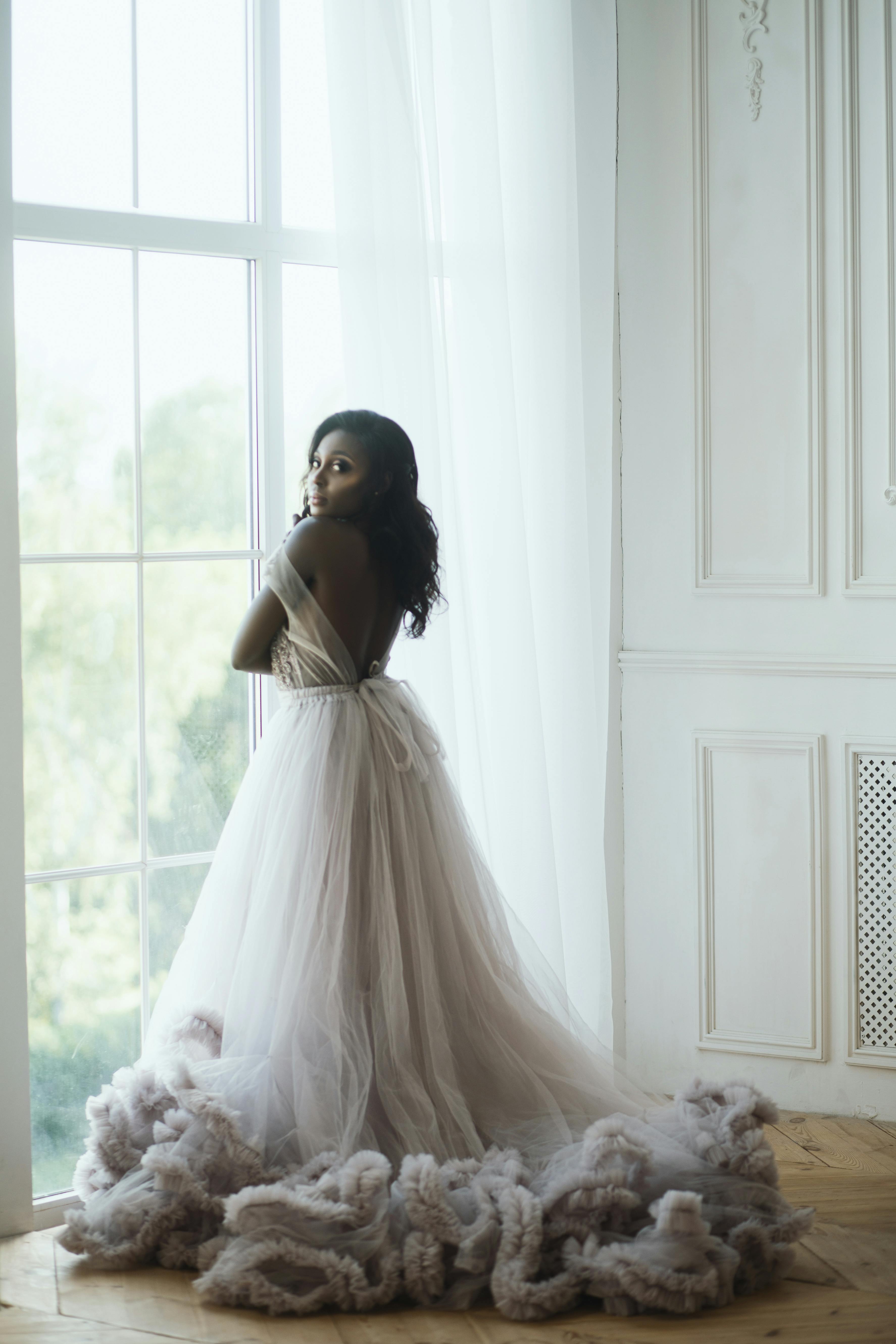 À des fins d'illustration uniquement. Une femme debout à une fenêtre en robe de mariée regarde l'appareil photo | Source : Pexels