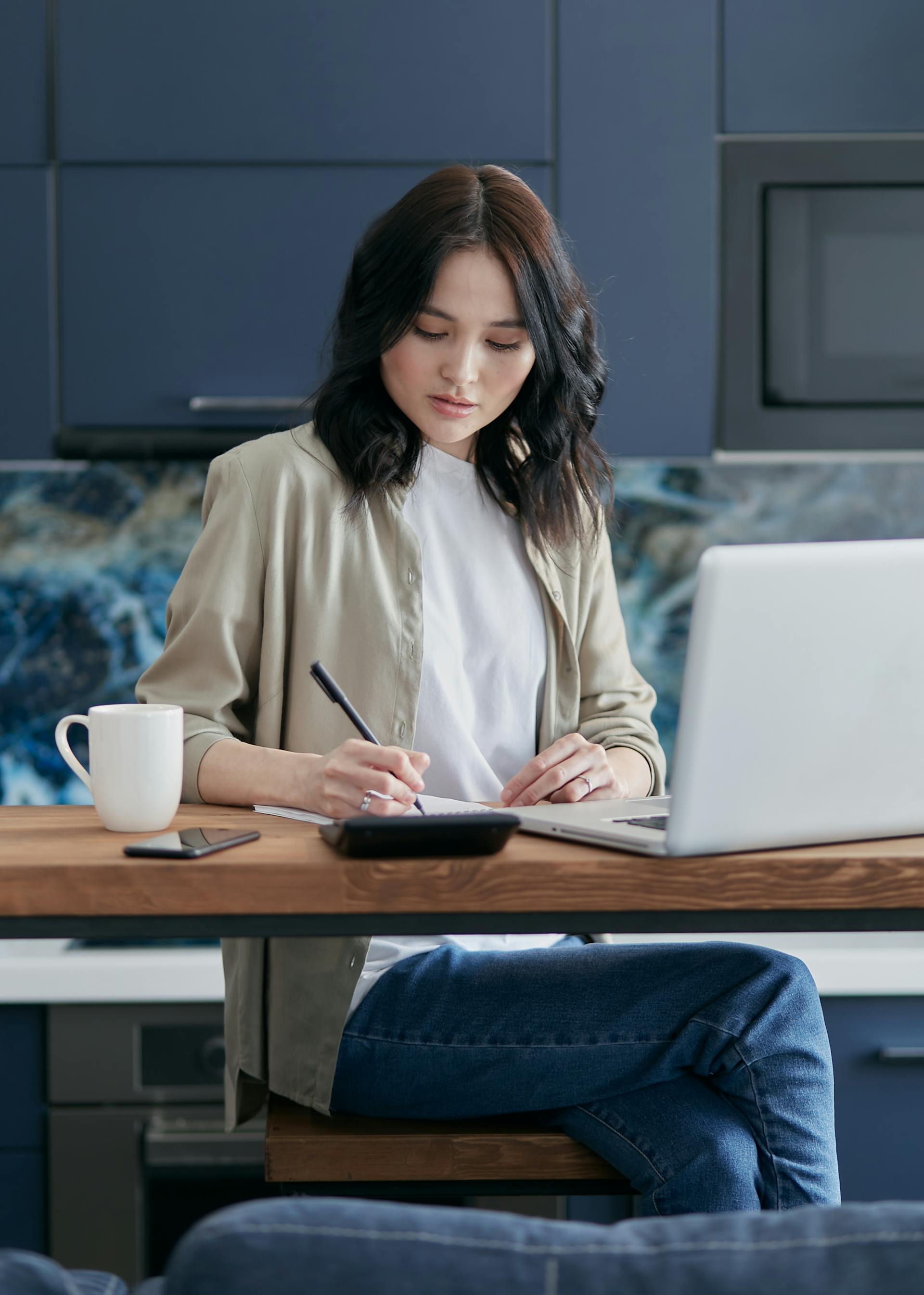 Une femme prend des notes tout en utilisant son ordinateur portable | Source : Pexels