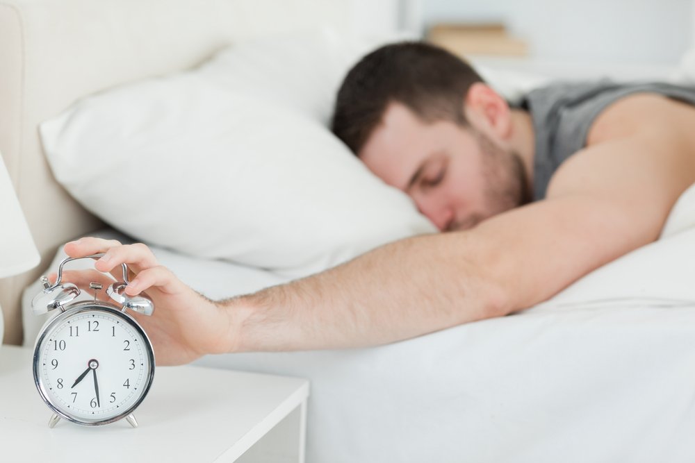Un homme épuisé, réveillé par un réveil dans sa chambre. | Shutterstock