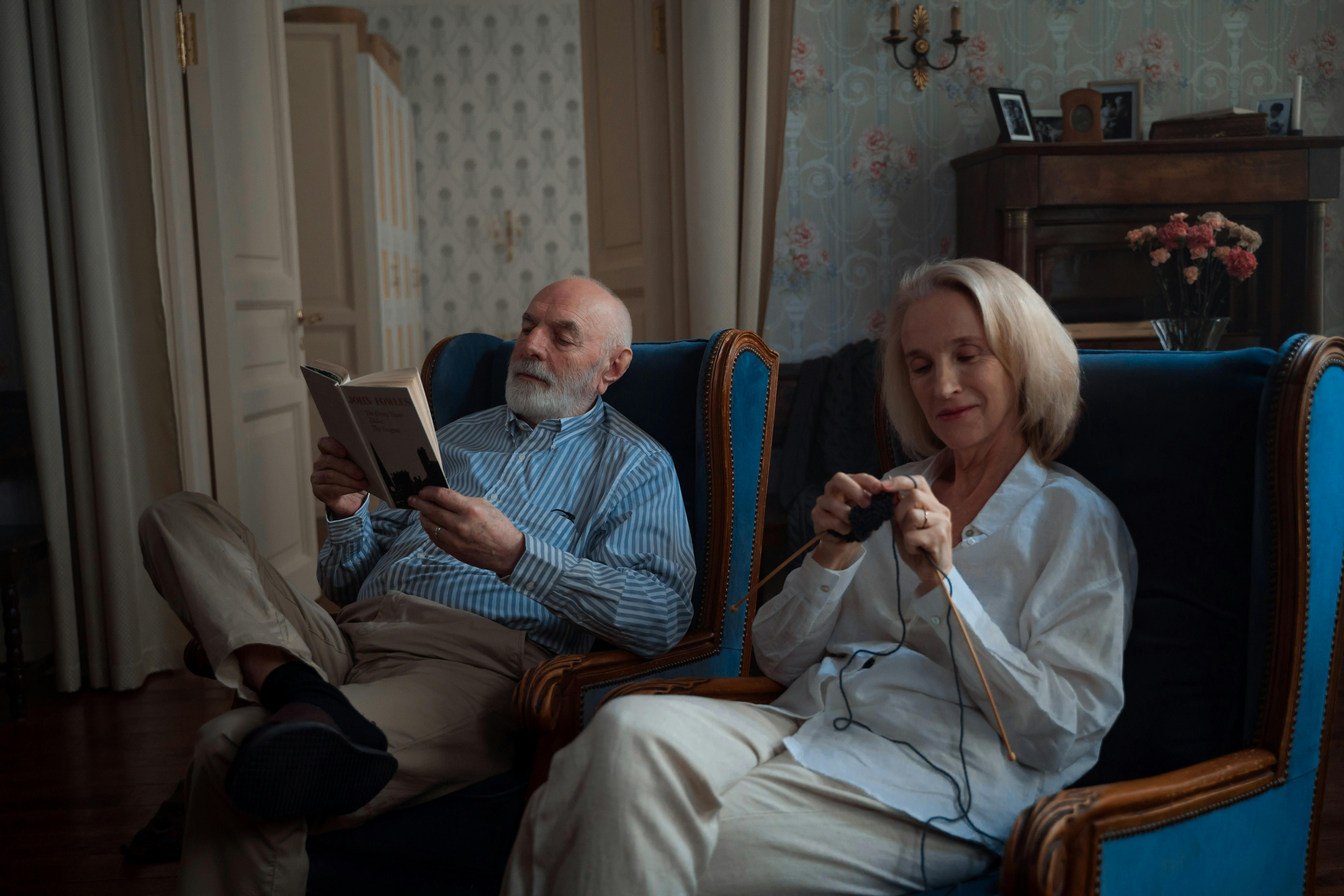 Un homme lisant un livre pendant que sa femme tricote joyeusement | Source : Pexels