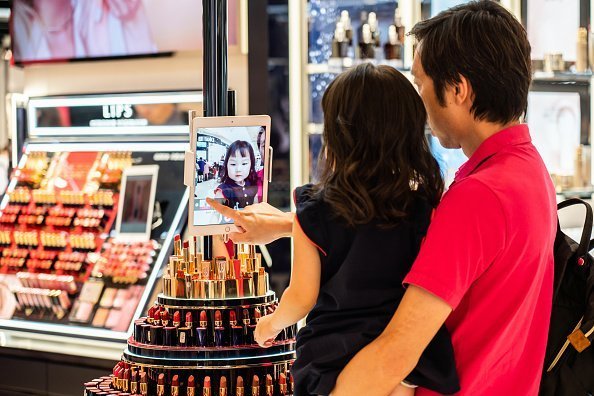 Père et fille jouant avec une tablette numérique dans un magasin Estée Lauder | Photo : Getty Images.