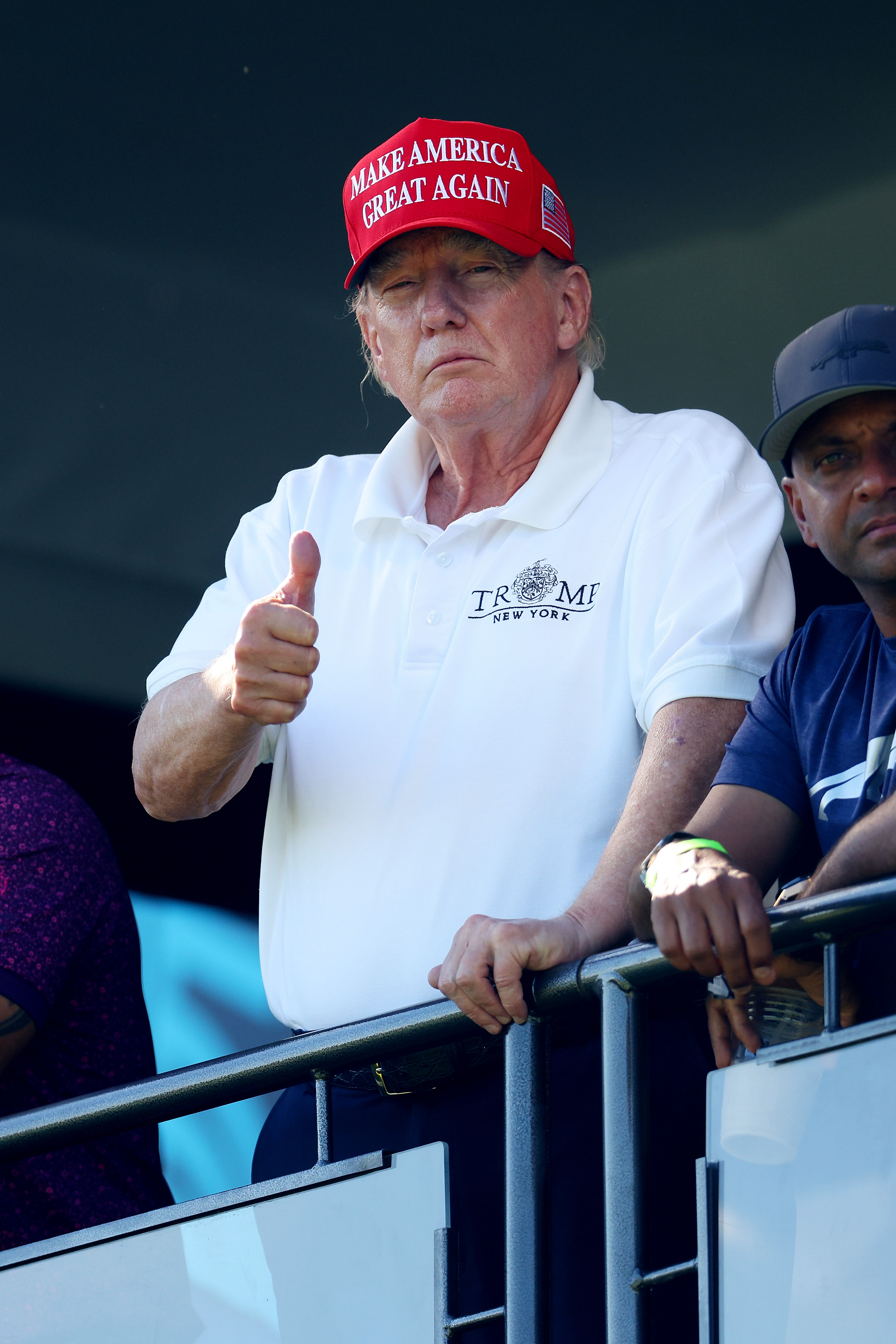 Le 13 août, Donald Trump se tient près d'une balustrade du 18e green, en train de lever le pouce. La rougeur de son visage reste visible, avec des tons plus clairs sur les bords de sa mâchoire et de son cou.
