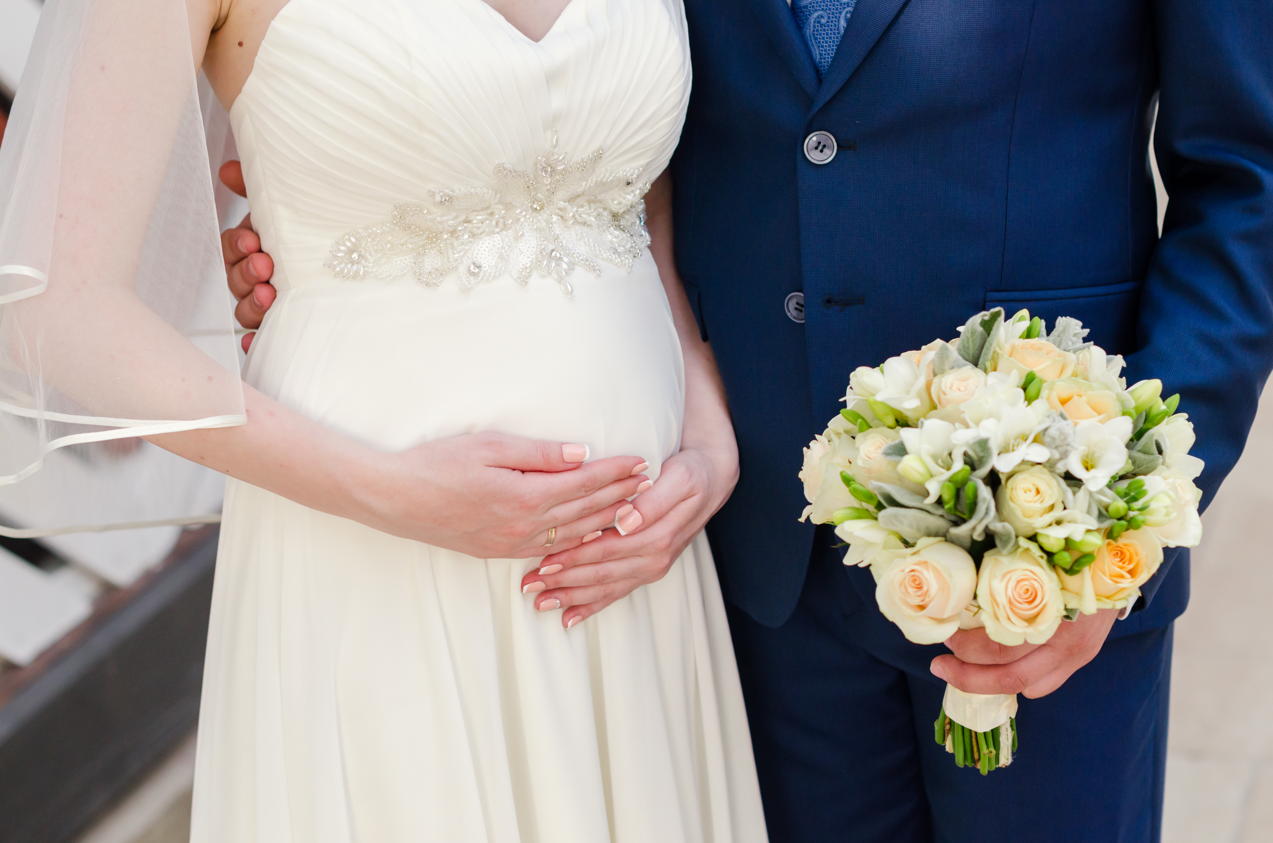 Une mariée enceinte tient son ventre pendant que son marié tient son bouquet | Source : Shutterstock