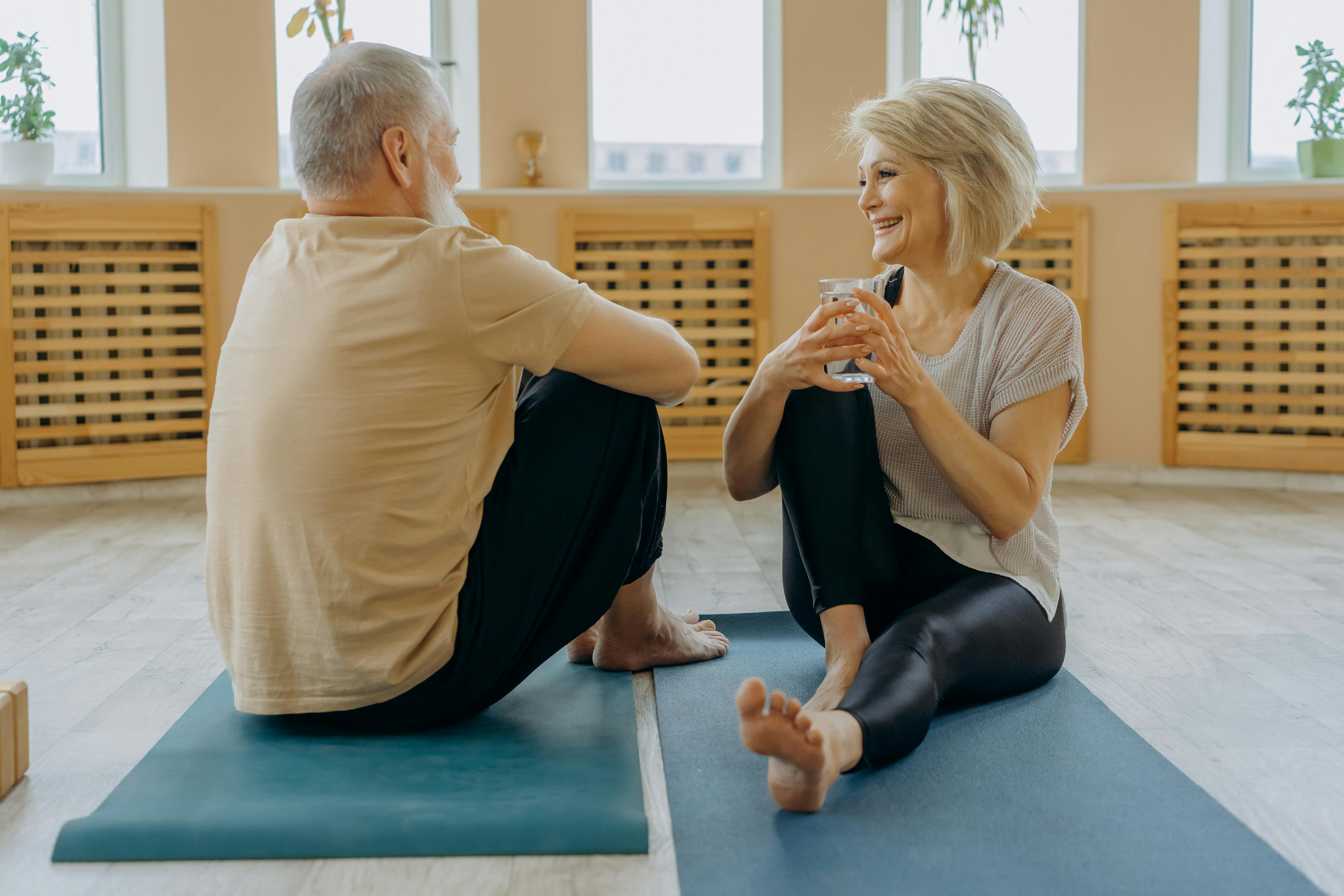 Un homme et une femme âgés ayant une conversation tout en étant assis sur un tapis de yoga | Source : Pexels