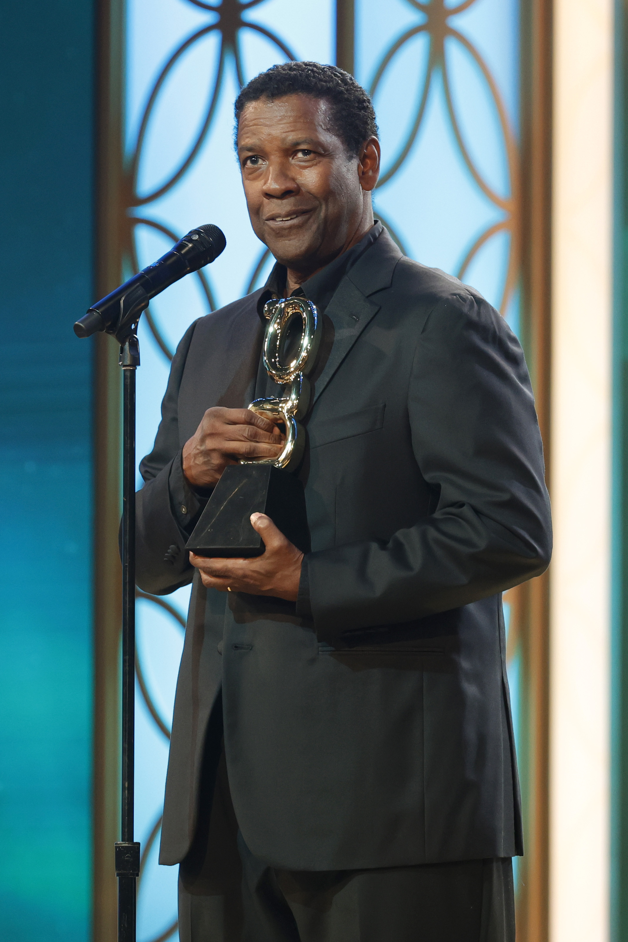 Denzel Washington reçoit le Film Icon Award lors des Grio Awards. Ses cheveux noirs sont légèrement coupés et bouclés. Vêtu d'un costume noir, son look mature et distingué reflète l'honneur qui lui a été rendu ce soir-là.
