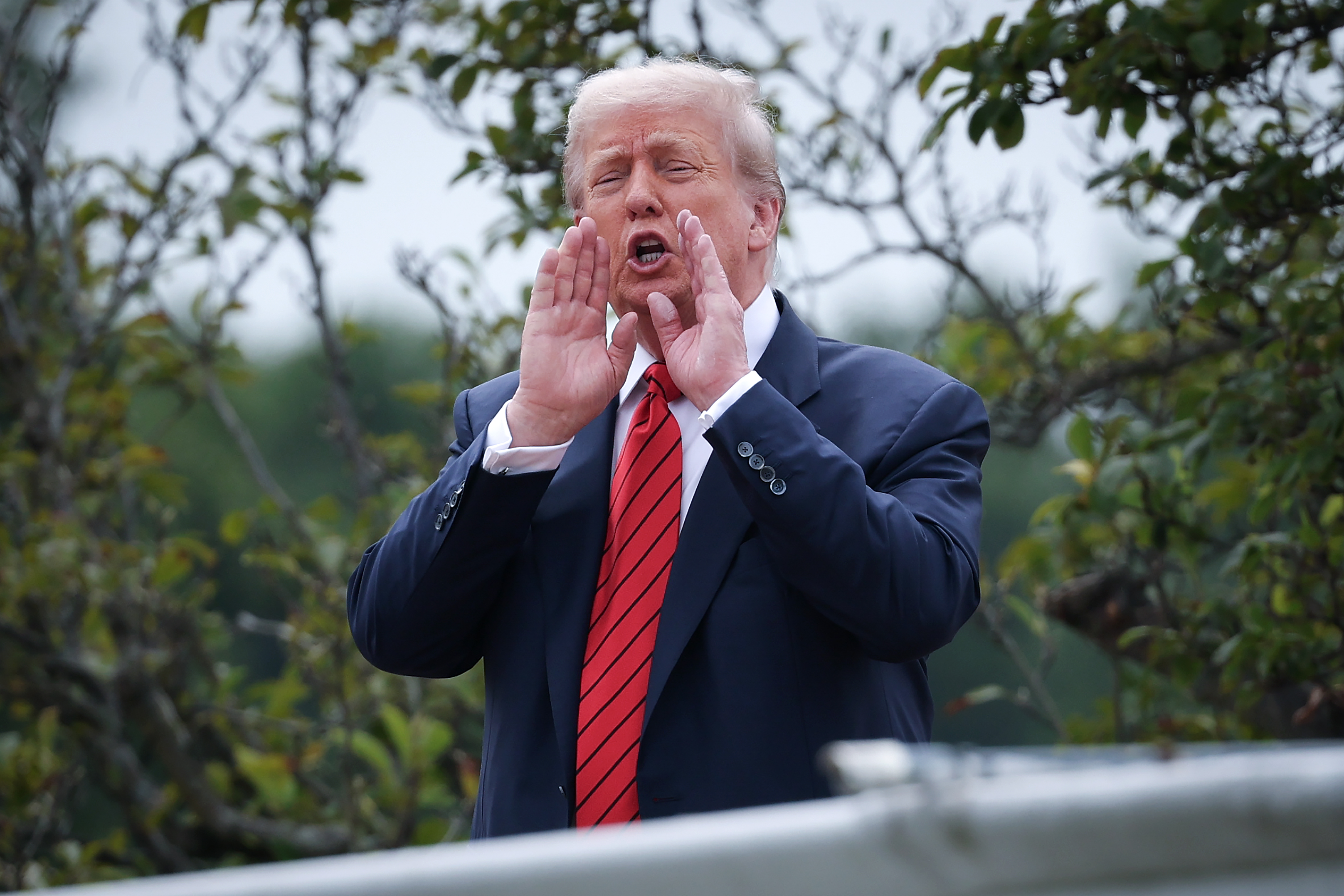 Le président Donald Trump met ses mains en porte-voix et s'adresse aux journalistes depuis le toit de l'aile ouest de la Maison Blanche à Washington, D.C., répondant aux questions avec enthousiasme.