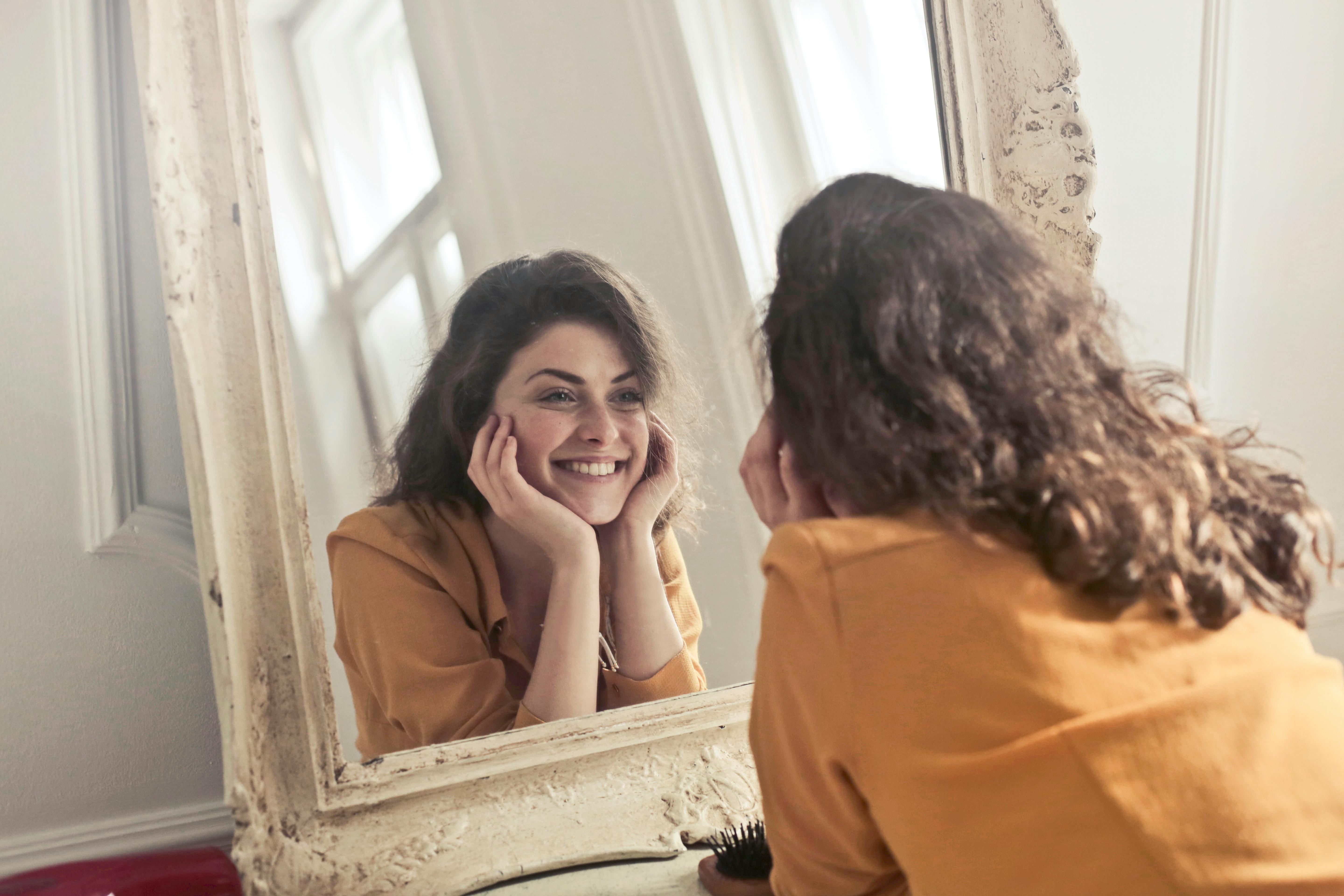 Une femme sourit en regardant son reflet dans un miroir | Source : Pexels