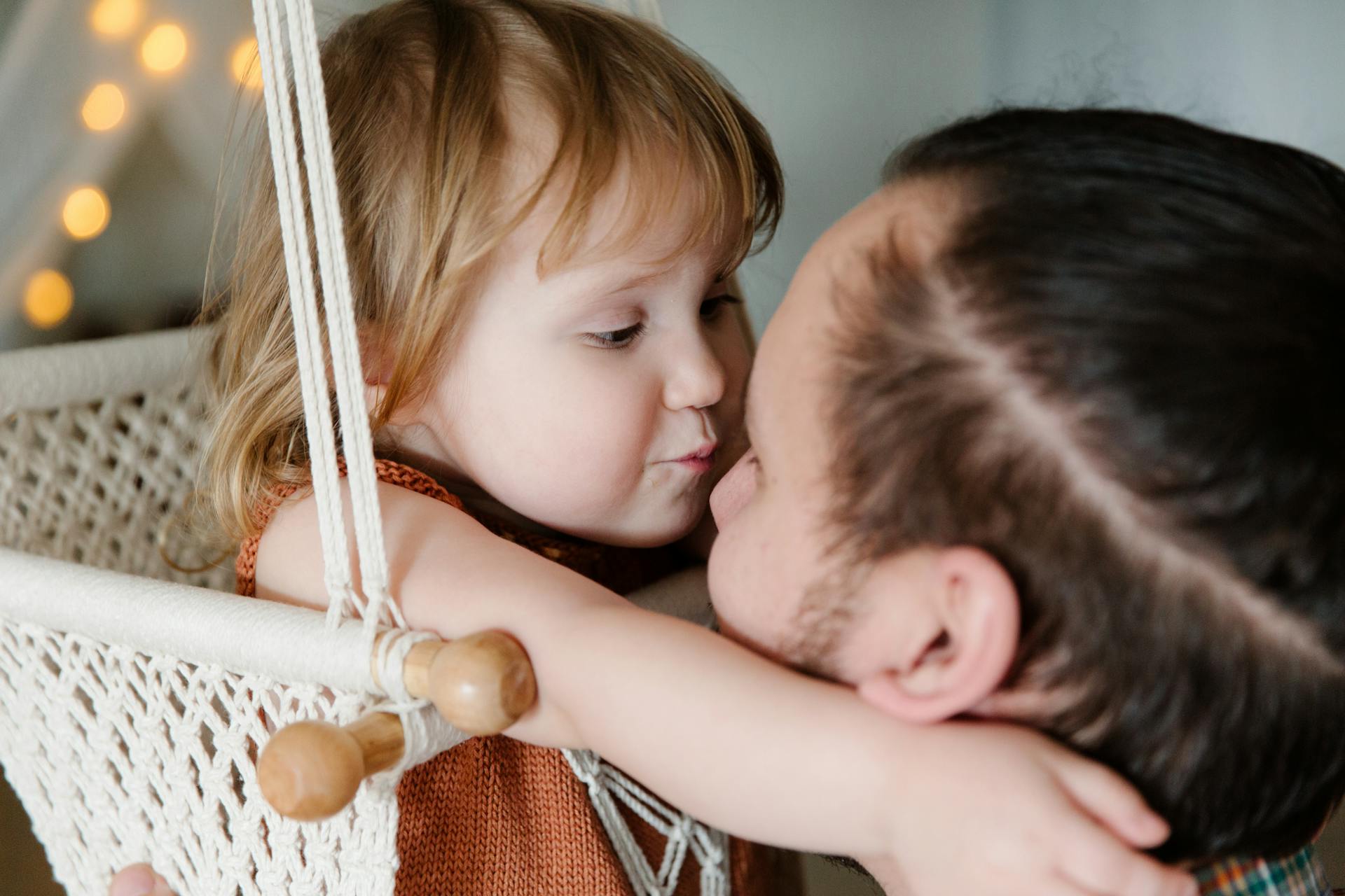 Une petite fille serrant son père dans ses bras tout en se reposant dans une balançoire suspendue | Source : Pexels