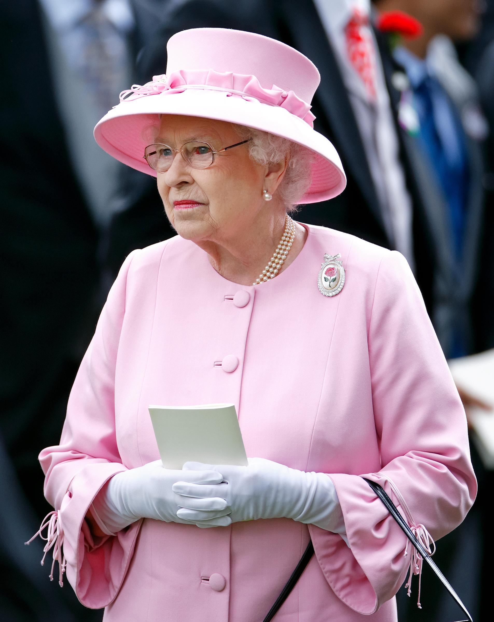 Tenant un objet et portant des gants blancs souples, l'élégance de la reine Elizabeth II resplendit lors de l'événement de 2012. Un œil rouge visible marque ce moment, offrant un rare aperçu de vulnérabilité au milieu de sa présence autrement posée.