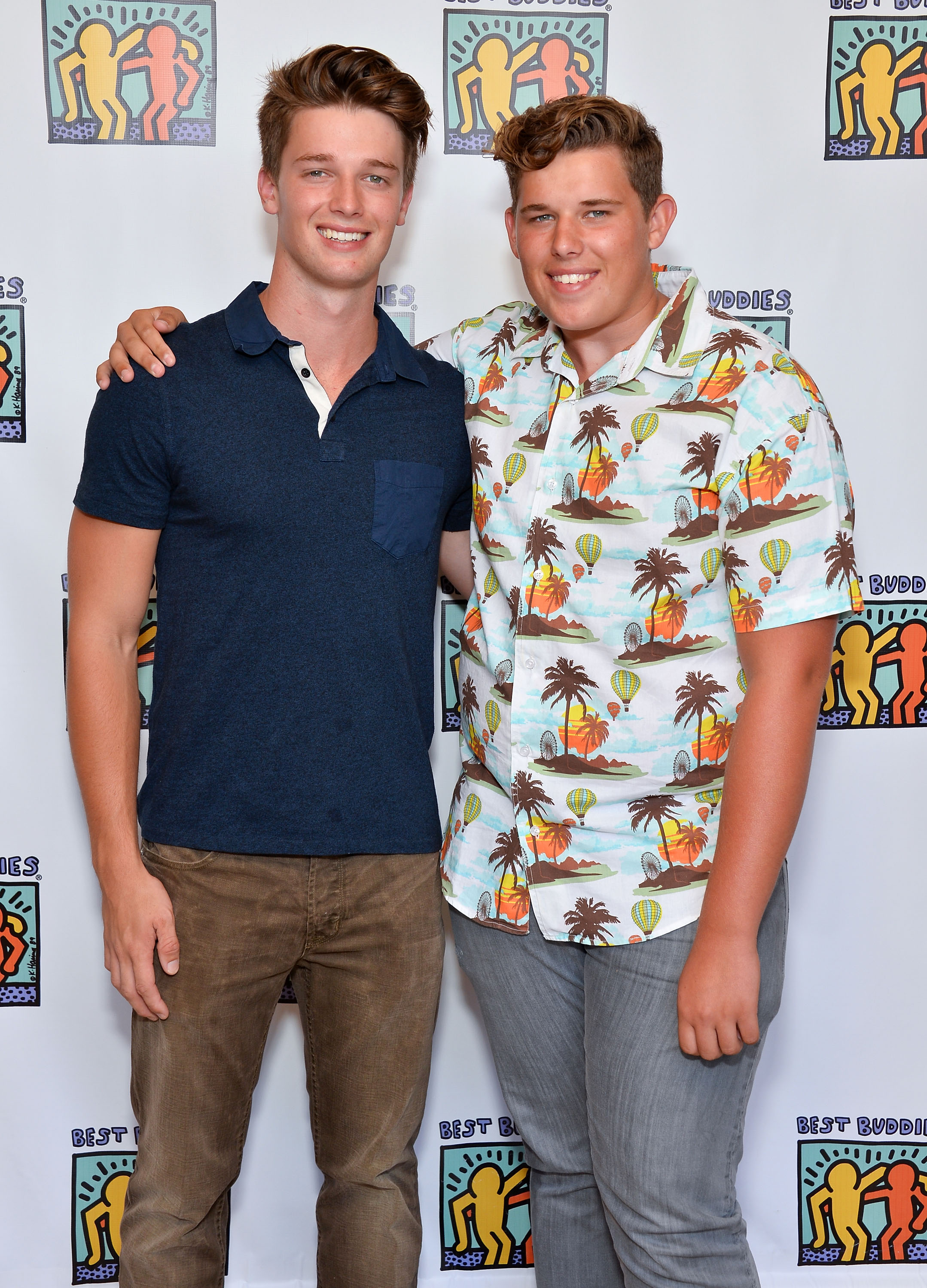 Patrick pose avec Christopher lors de la soirée de charité Team Maria au profit de Best Buddies à Beverly Hills. Patrick reste simple avec un polo bleu marine et un jean marron, tandis que Christopher se démarque avec une chemise à boutons colorée à imprimé tropical et un pantalon gris.