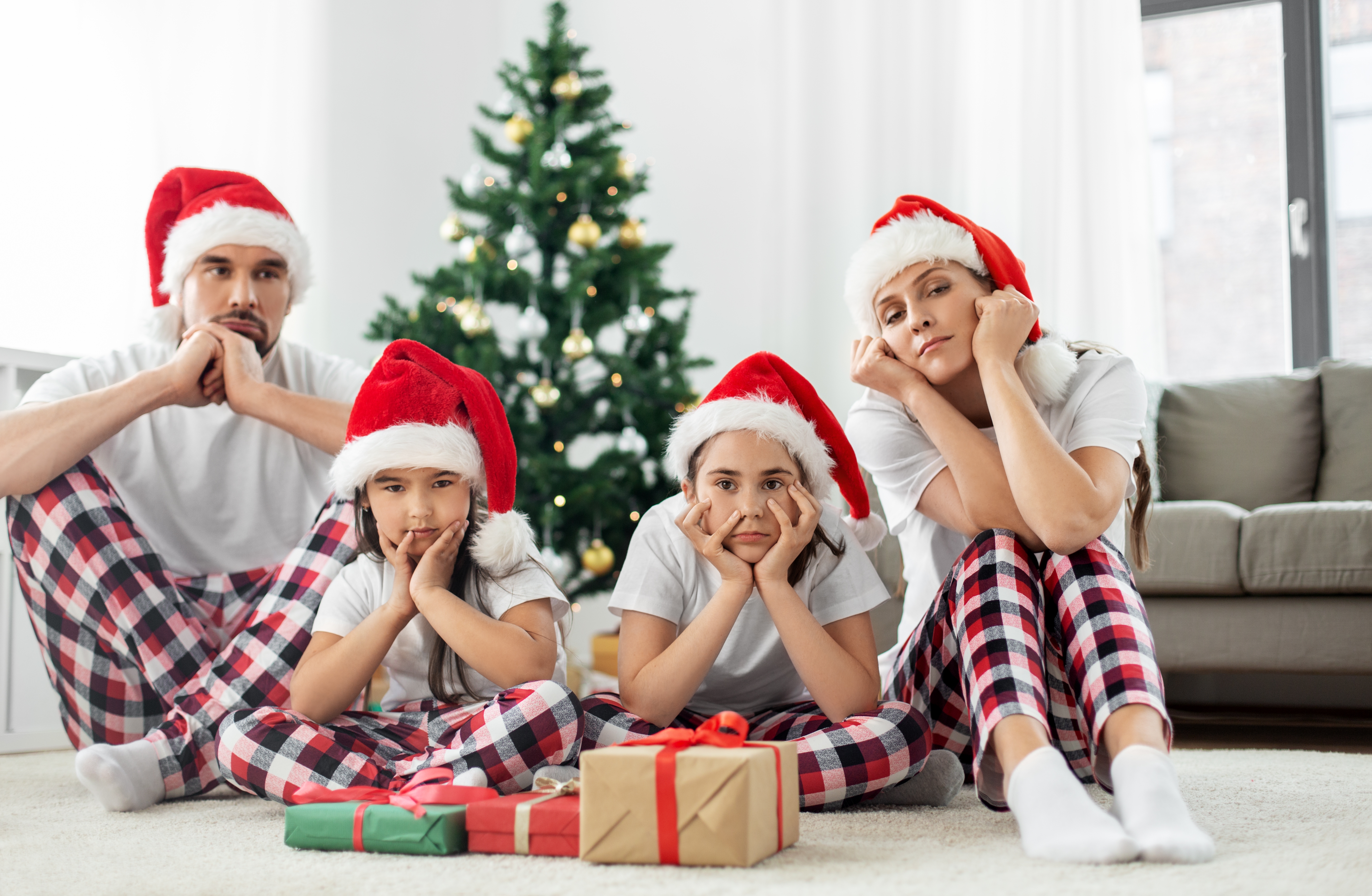 Une famille déprimée de quatre personnes assise près d'un arbre de Noël et portant des bonnets de Père Noël | Source : Shutterstock