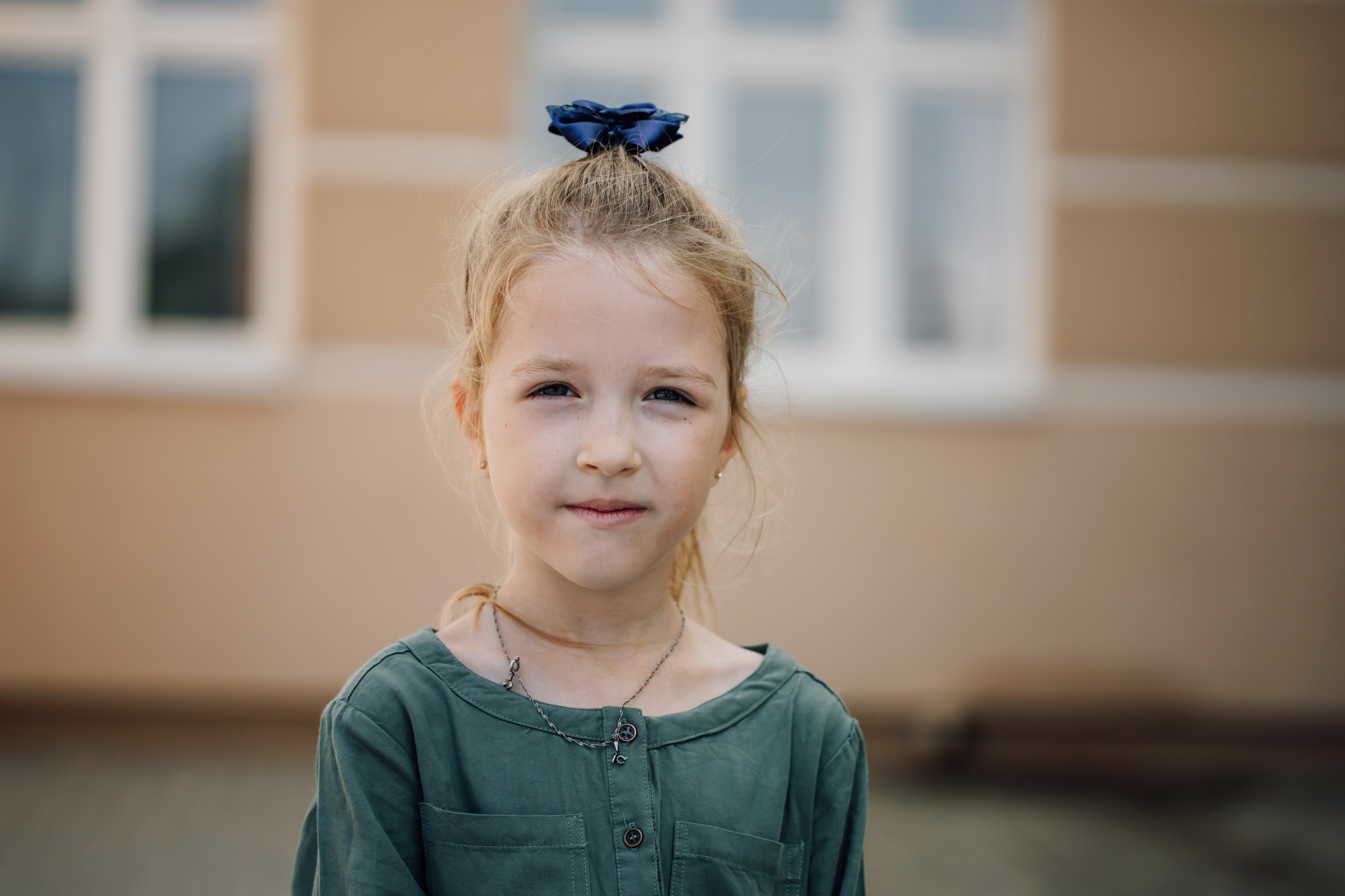 Portrait d'une petite fille sérieuse qui regarde l'appareil photo avec un bâtiment d'école primaire en arrière-plan | Source : Getty Images