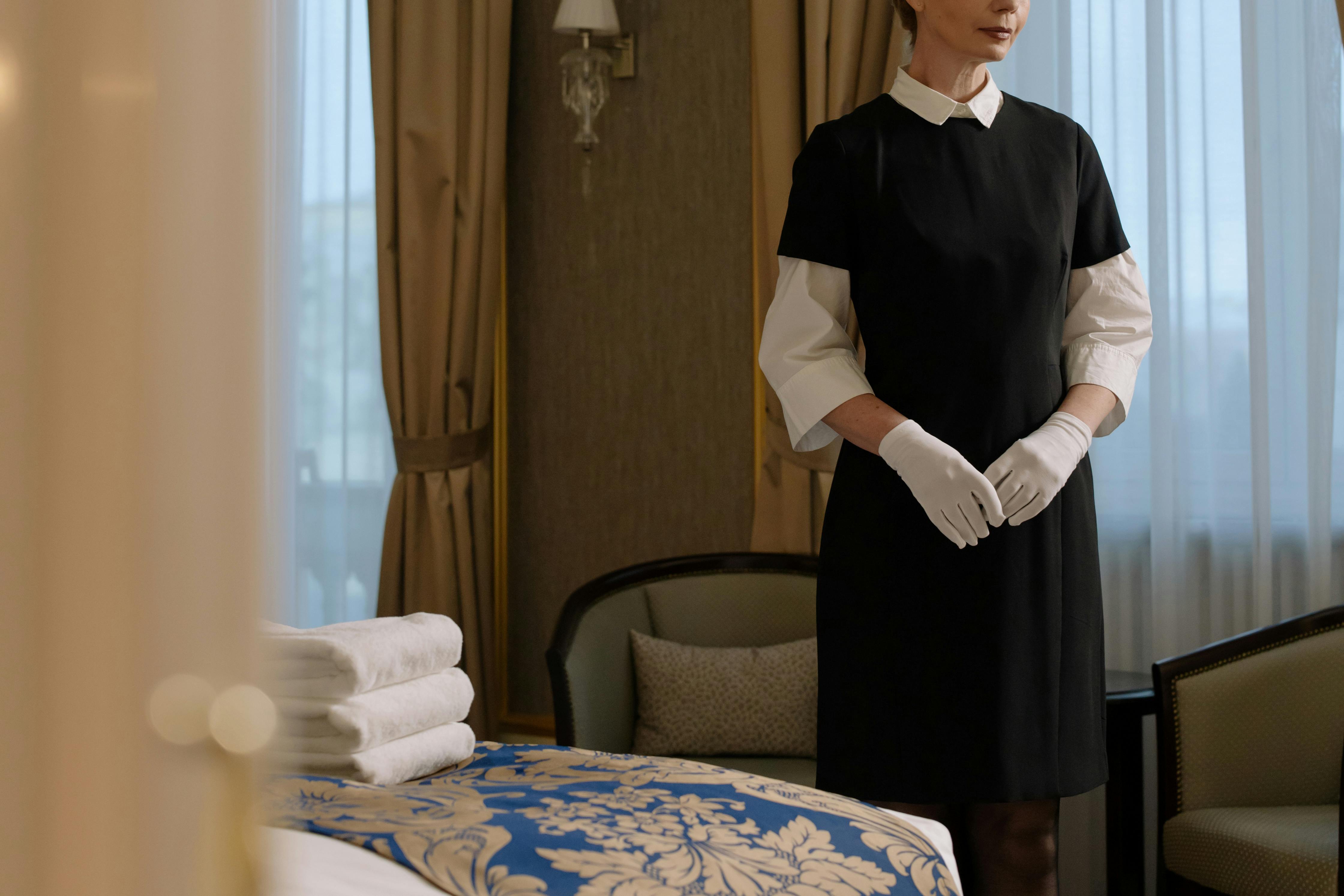 Femme en uniforme à côté du lit d'une chambre d'hôtel | Source : Pexels