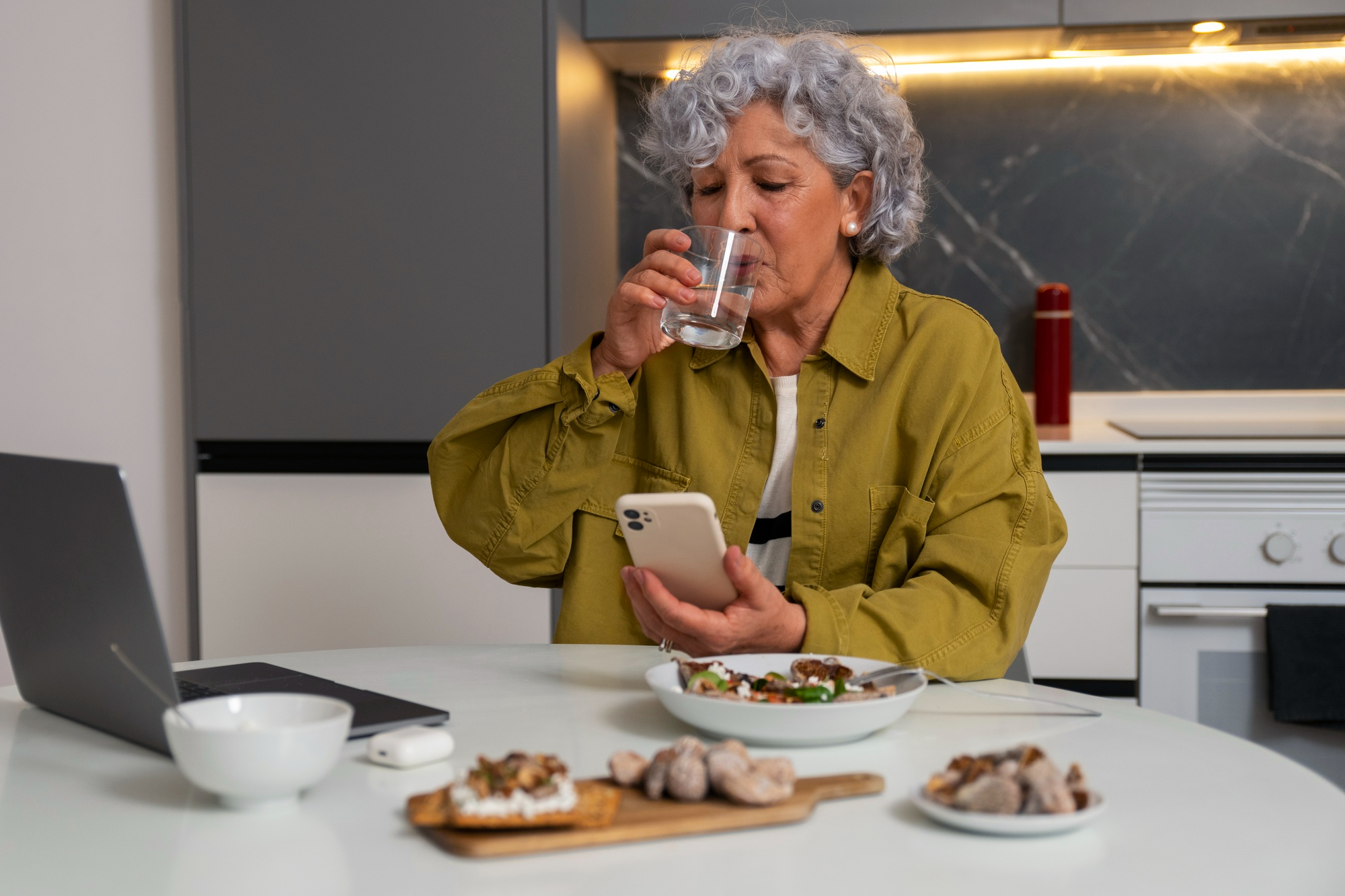 Une femme assise dans la cuisine en train de déguster un repas et de regarder son téléphone. | Source : Freepik