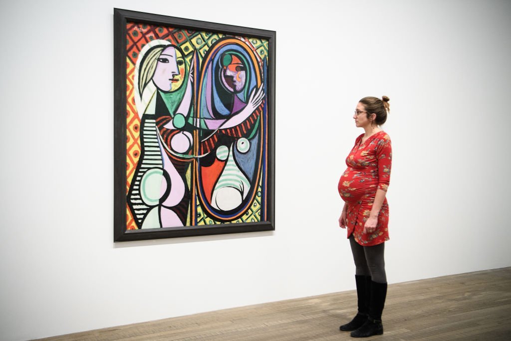 Une femme enceinte regarde "Girl before a Mirror" de Pablo Picasso au Tate Modern le 6 mars 2018 à Londres, en Angleterre. "Picasso 1932 : Love, Fame and Tragedy" est la première exposition personnelle de l'artiste à la Tate Modern et comprend plus de 100 œuvres.| Source : Getty Images.