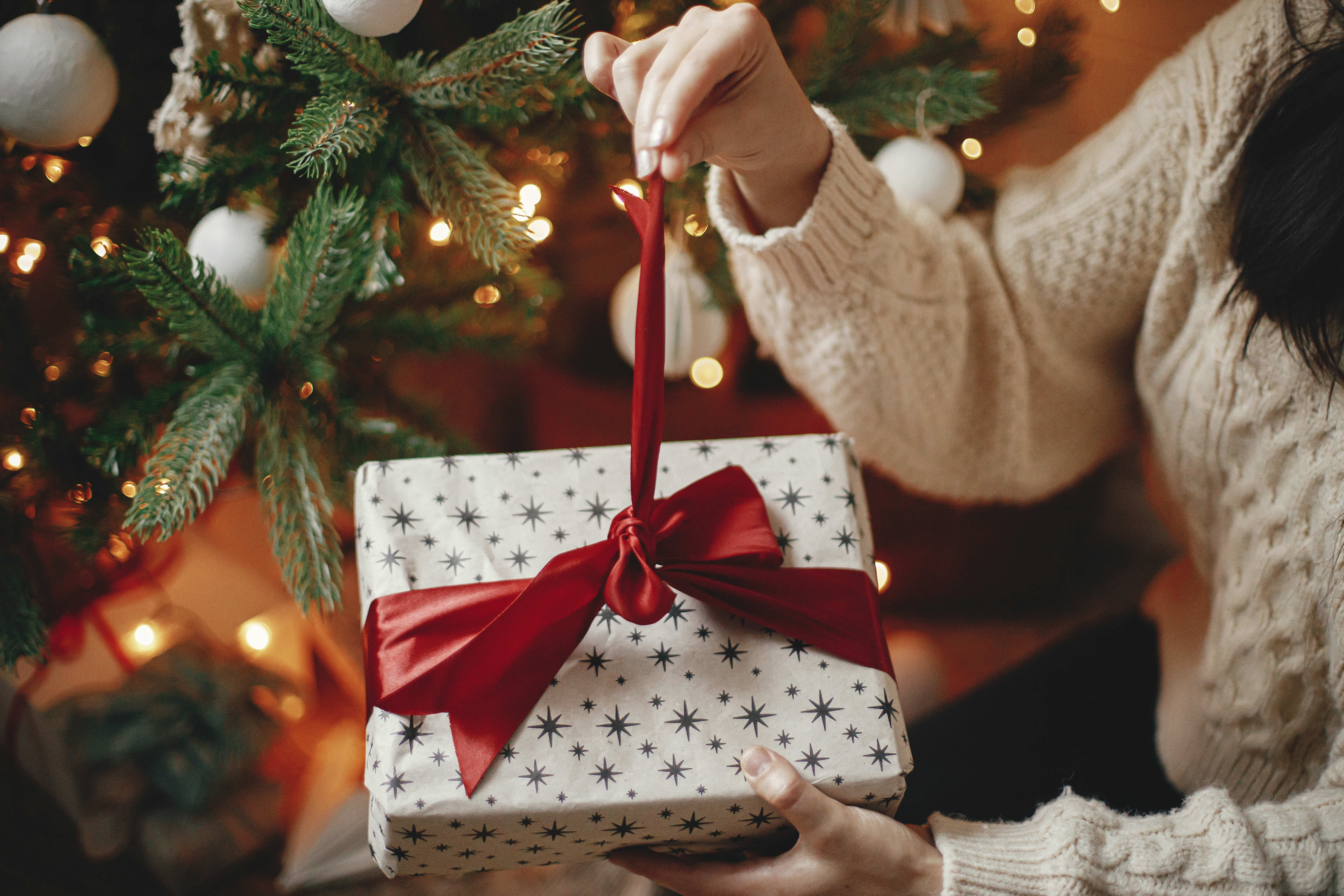 Les mains dans un pull douillet en train d'ouvrir un cadeau de Noël | Source : Shutterstock