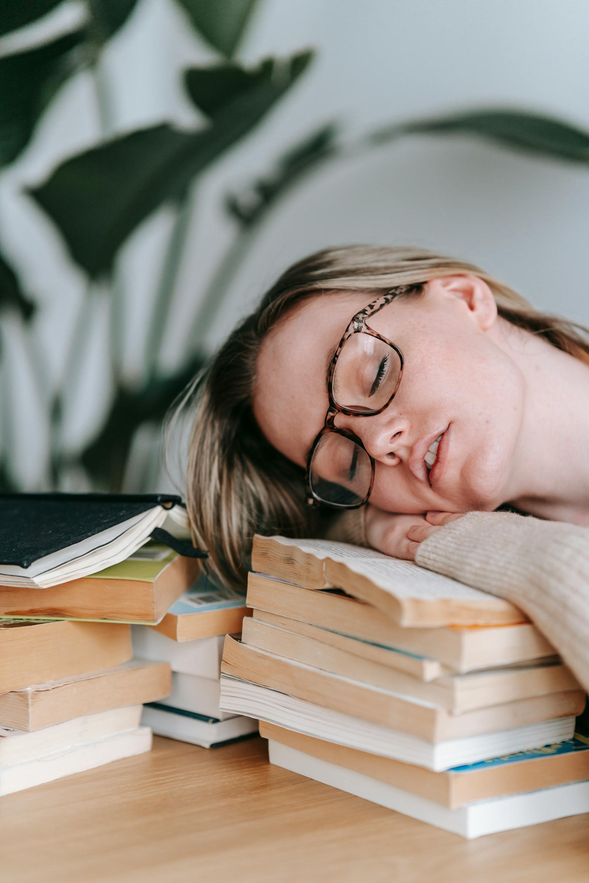 Une jeune femme fatiguée reposant sa tête sur une pile de livres | Source : Pexels