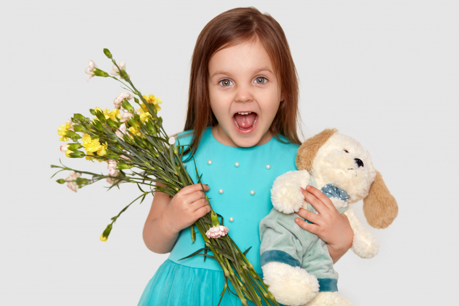 Une petite fille ravie tenant des fleurs et une peluche | Source : Freepik