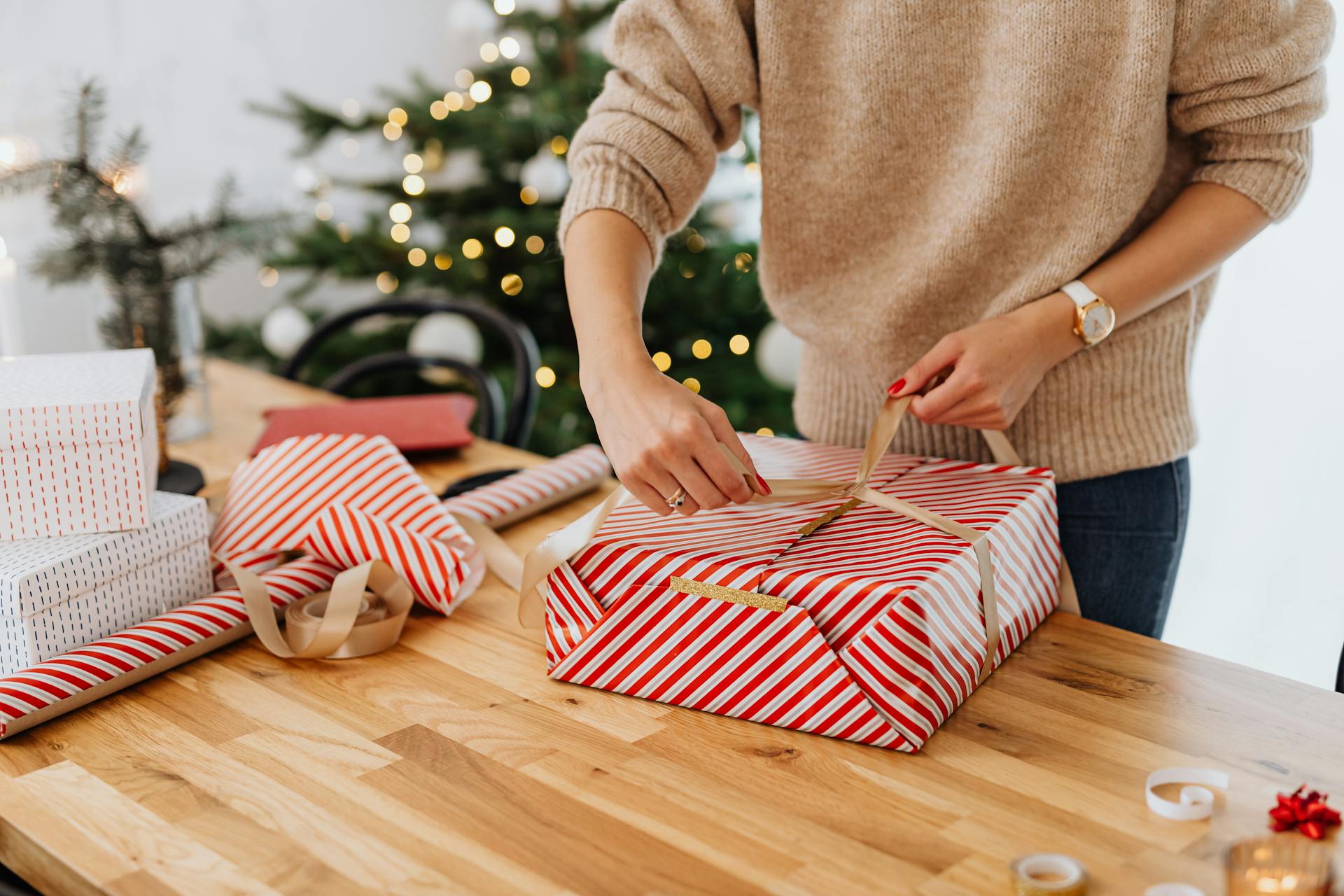 Une femme emballe un cadeau avec un arbre de Noël en arrière-plan | Source : Pexels