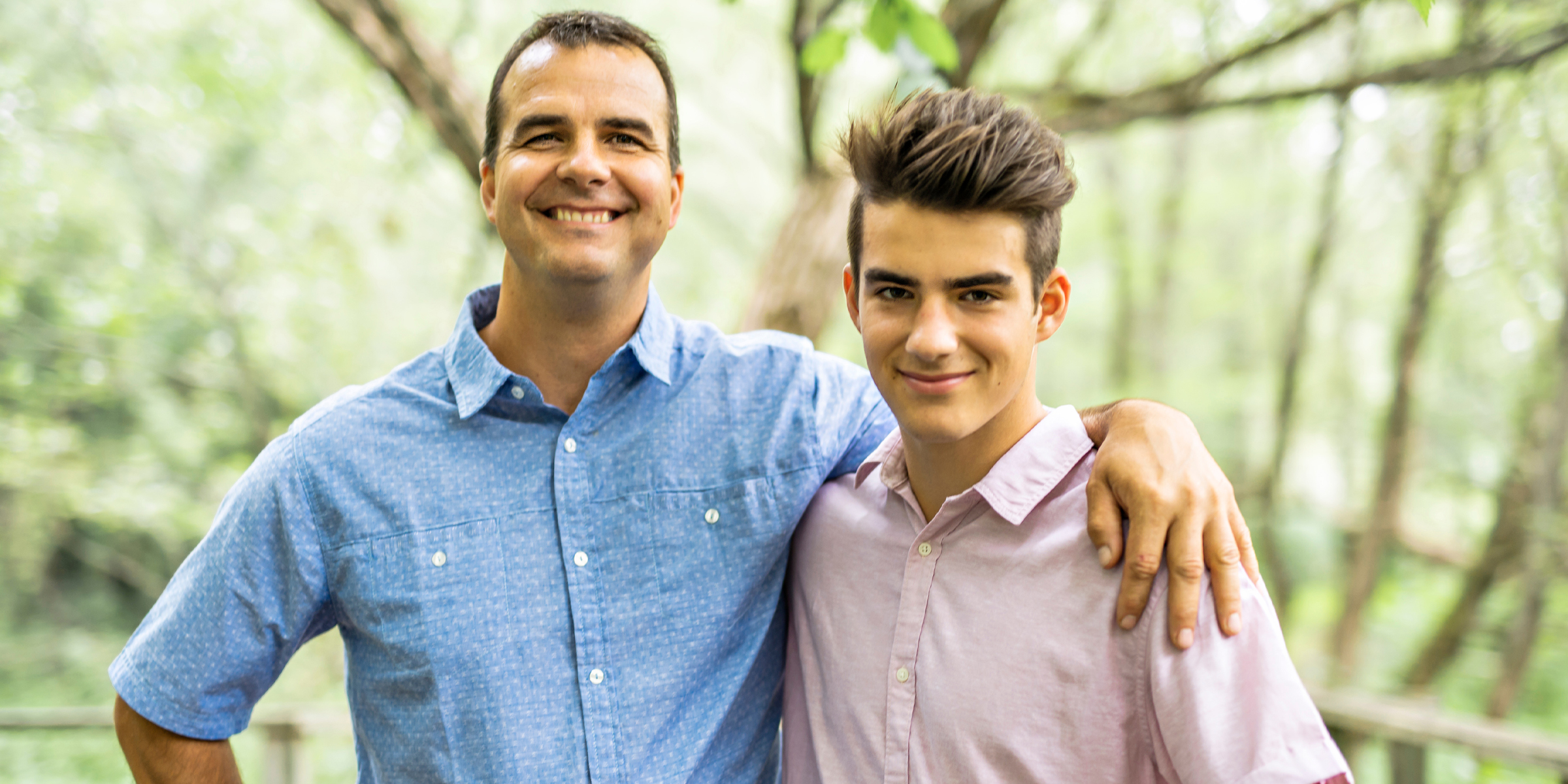 Un homme souriant et un adolescent posant ensemble à l'extérieur dans une zone boisée | Souce : Shutterstock