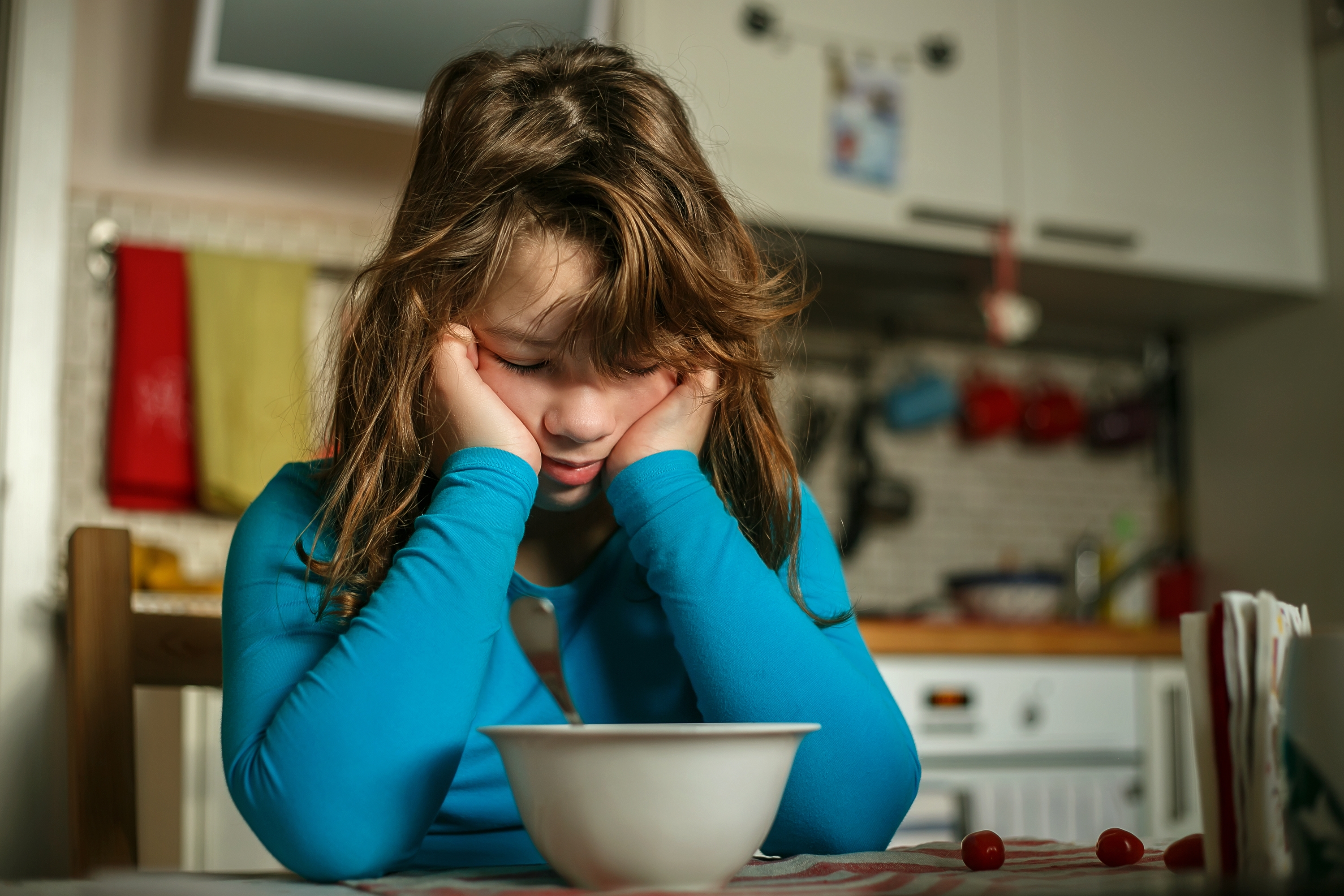 Menina se inclina sobre um prato do café da manhã em uma pose descontente | Fonte: Shutterstock.com