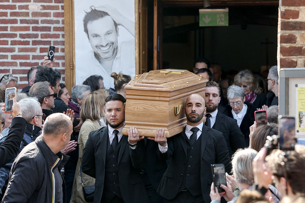 Une foule de personnes en deuil regarde le cercueil être transporté hors de l'église Sainte-Anne de Polangis lors des funérailles de Bruno Salomone, le 23 mars 2026 à Joinville-le-Pont, en France I Source : Getty Images