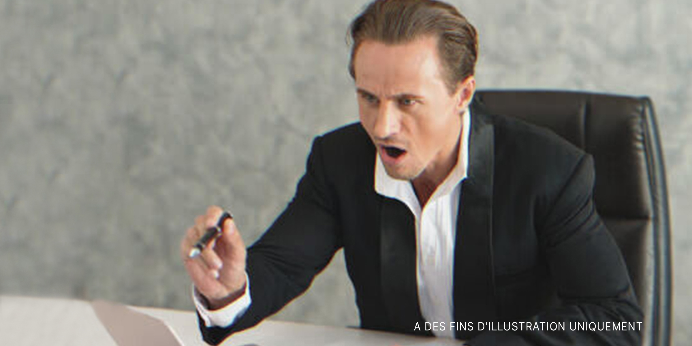 Homme assis sur un bureau, pointant du doigt avec colère. | Source : Shutterstock