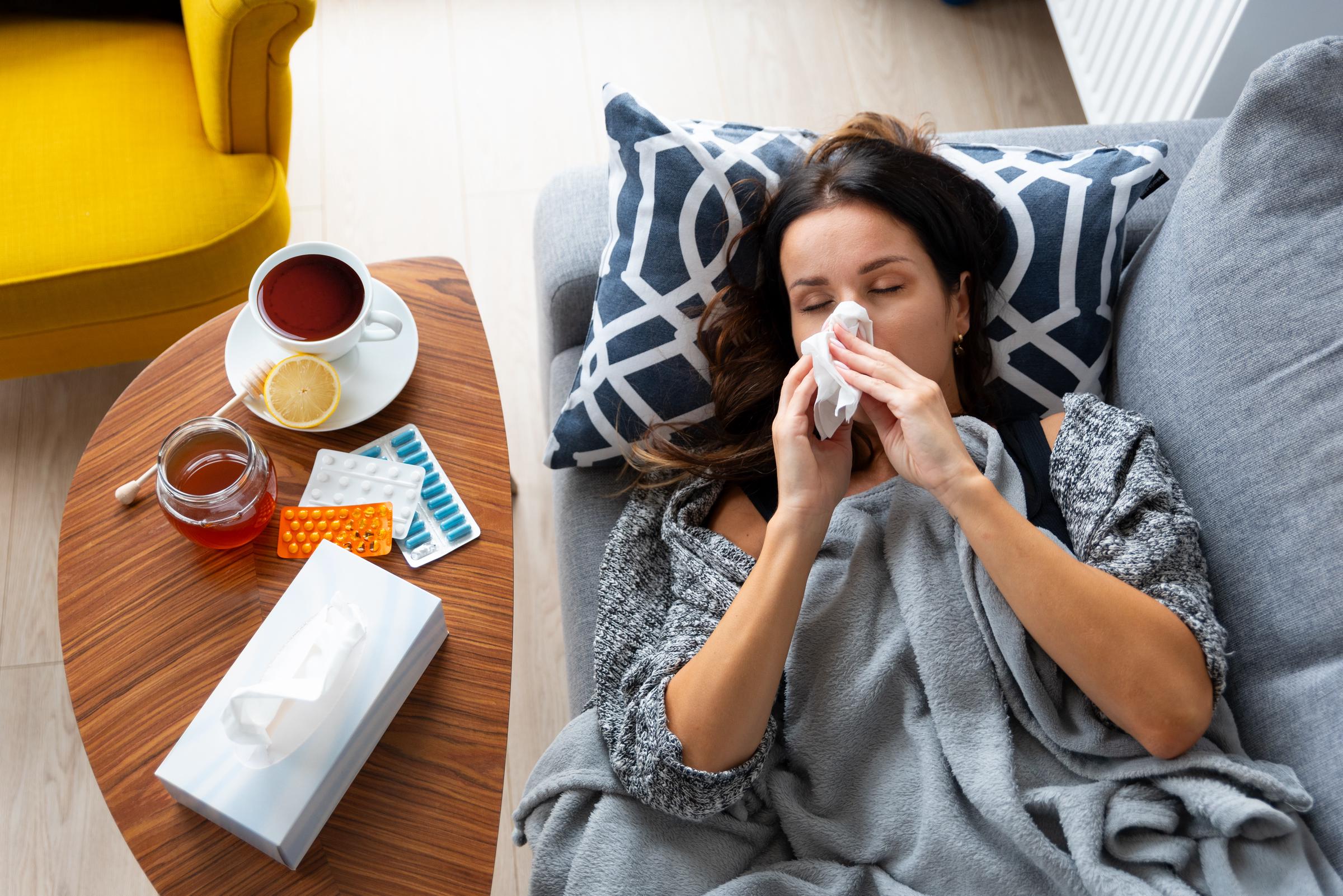 Une femme malade se repose sur le canapé, en gérant les symptômes du rhume ou de la grippe avec des médicaments et des remèdes courants pour les infections des voies respiratoires supérieures | Source : Getty Images