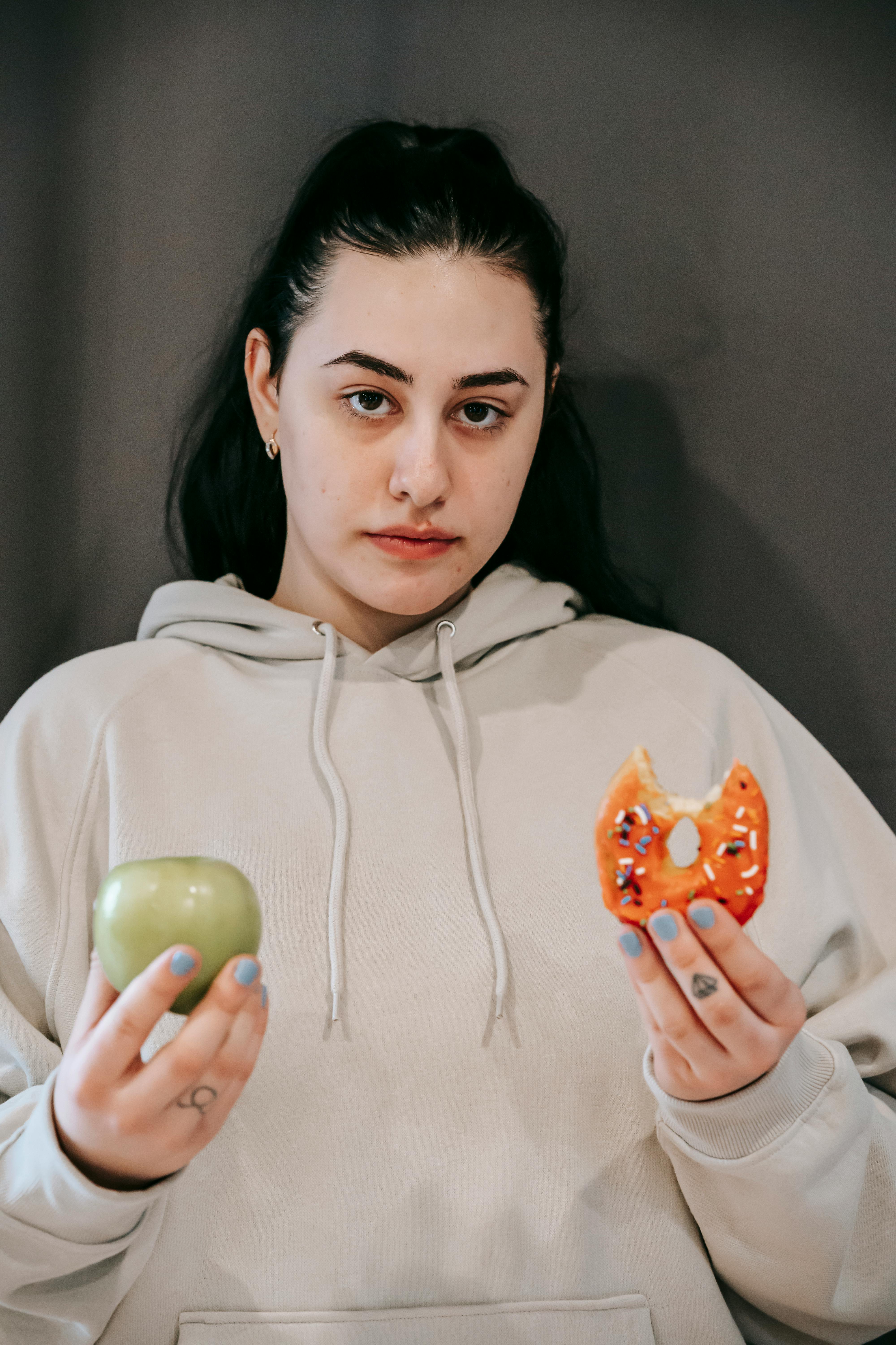 Une femme tenant une pomme et un beignet | Source : Pexels