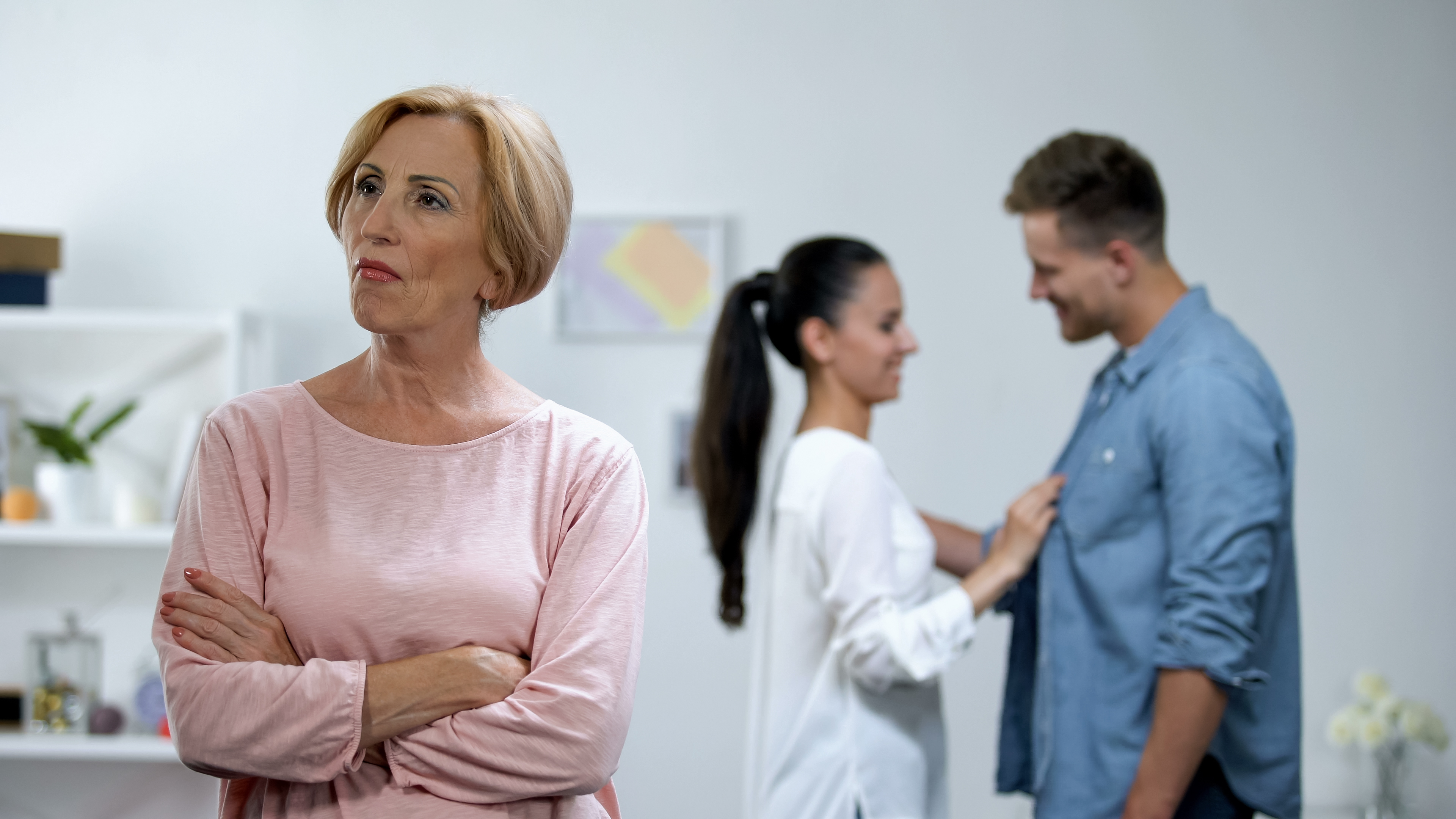 Une belle-mère debout, les bras croisés, avec son fils et sa belle-fille semblant heureux en arrière-plan | Source : Shutterstock