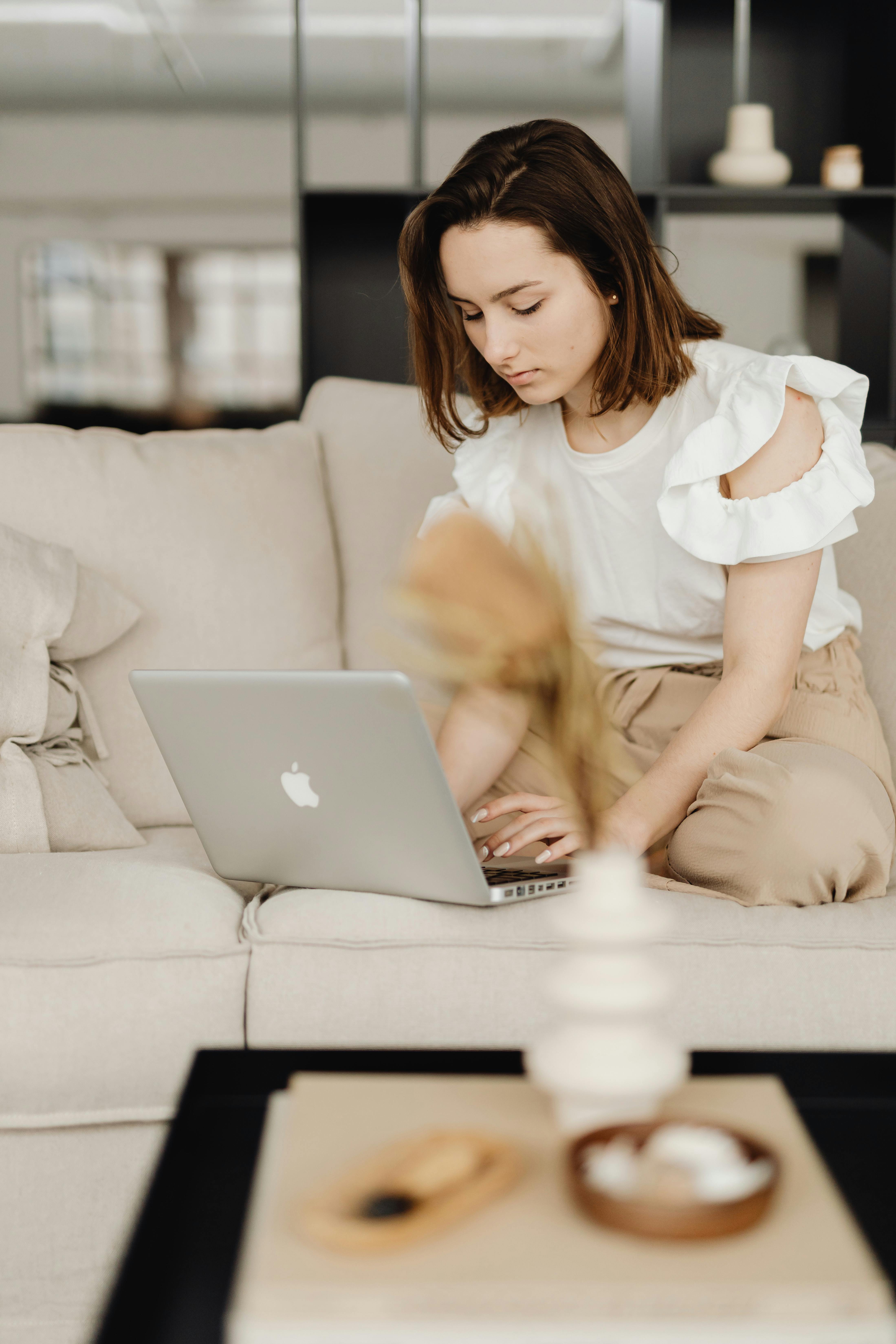 Une femme sur le canapé en train de taper sur un Macbook | Source : Pexels