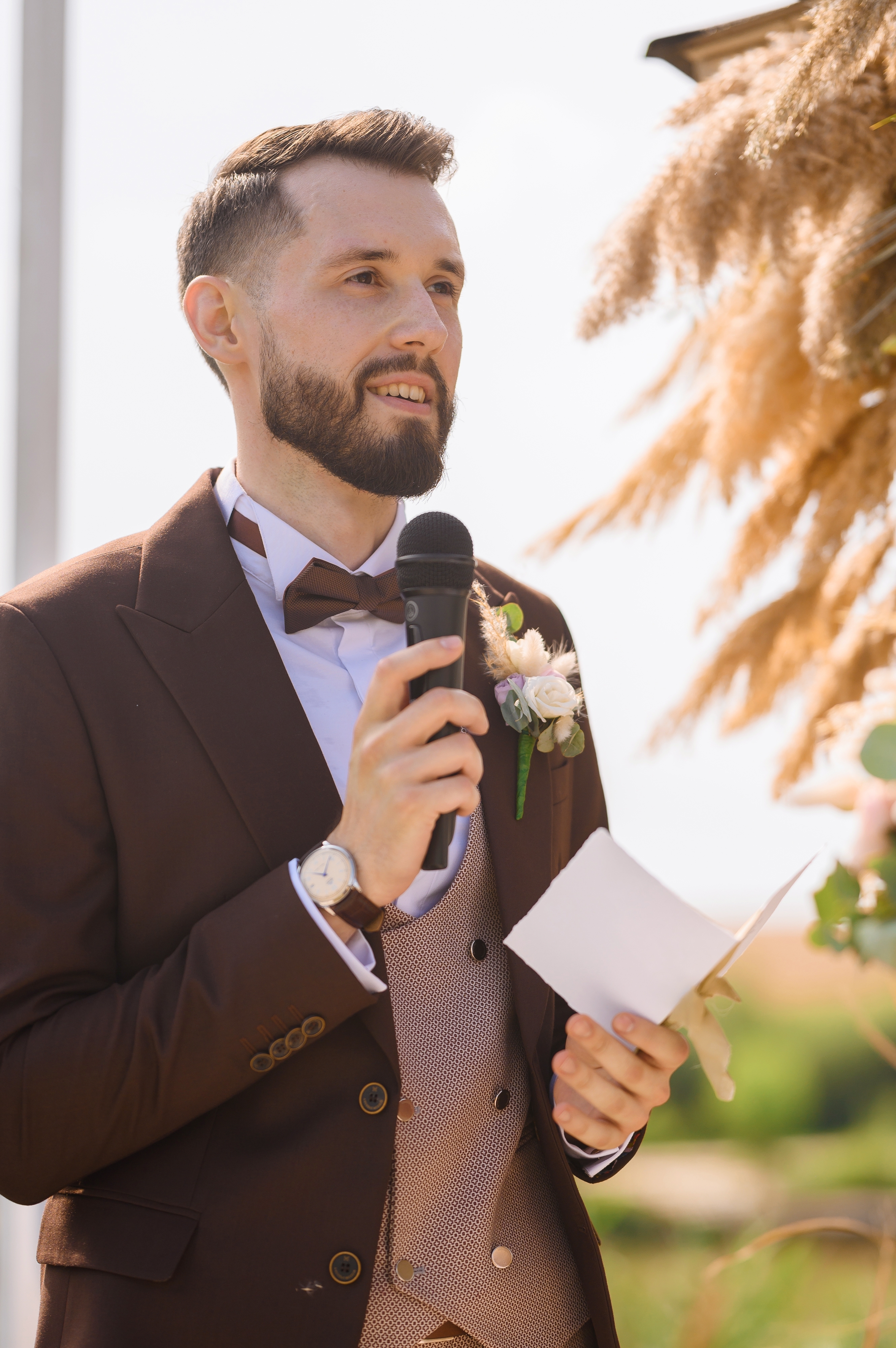 Un homme vêtu d'un costume marron avec une boutonnière et un nœud papillon prononçant un discours lors d'un mariage | Source : Shutterstock