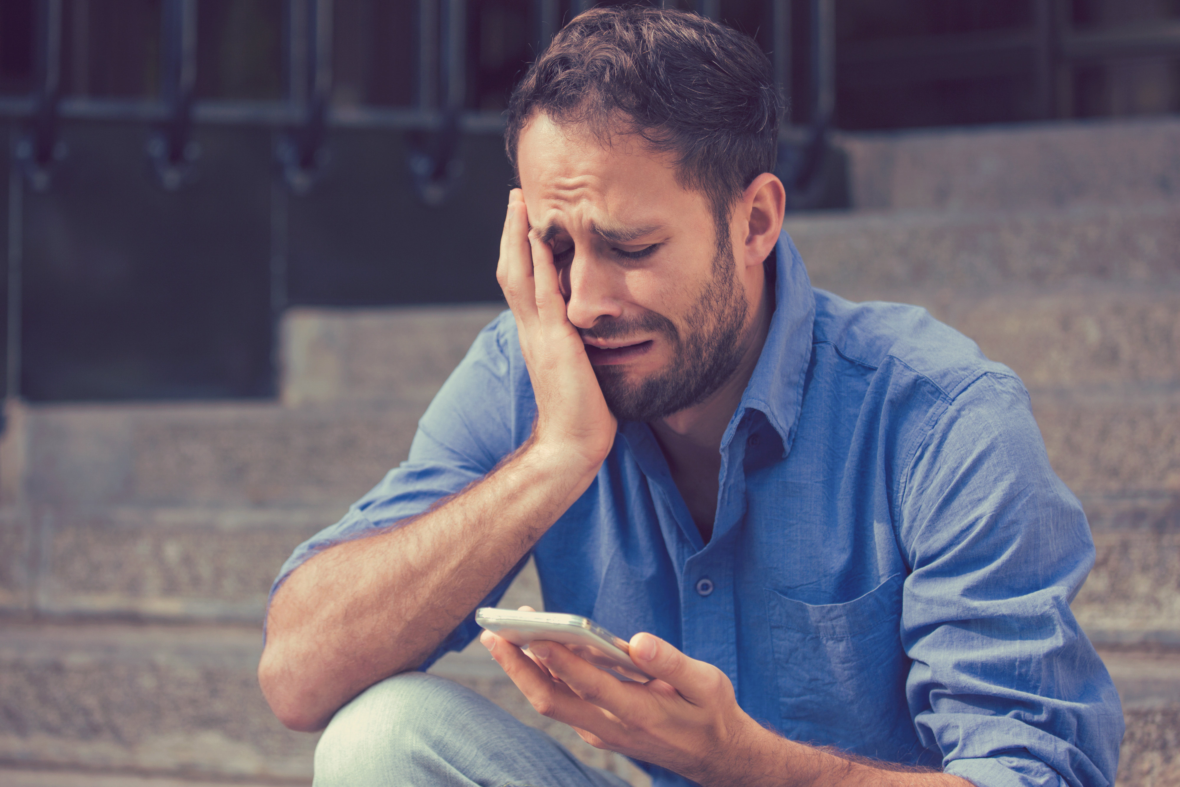 Un homme sanglote en fixant son téléphone portable | Source : Shutterstock