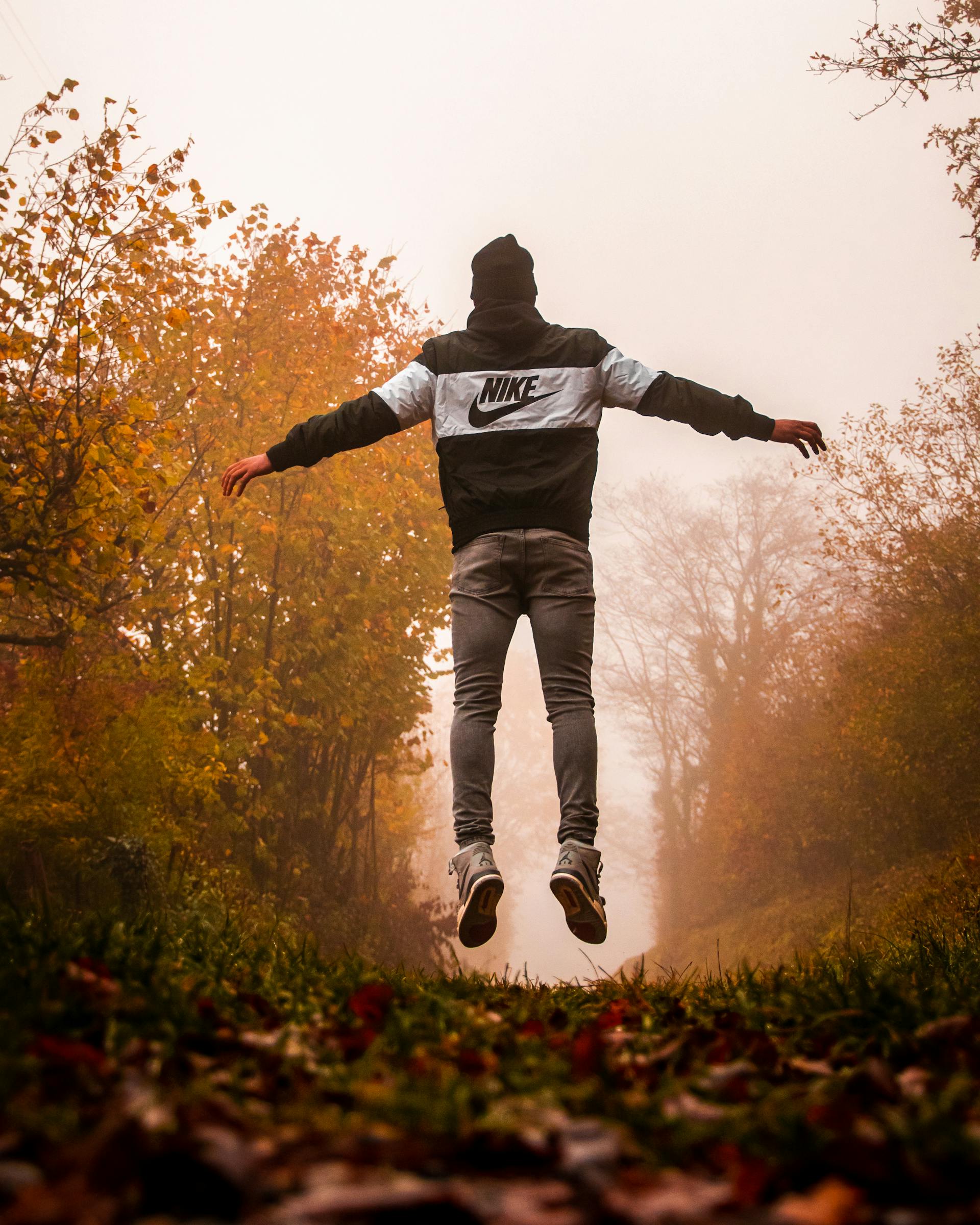 Un homme vêtu d'un sweat à capuche Nike et d'un pantalon gris sautant en l'air | Source : Pexels