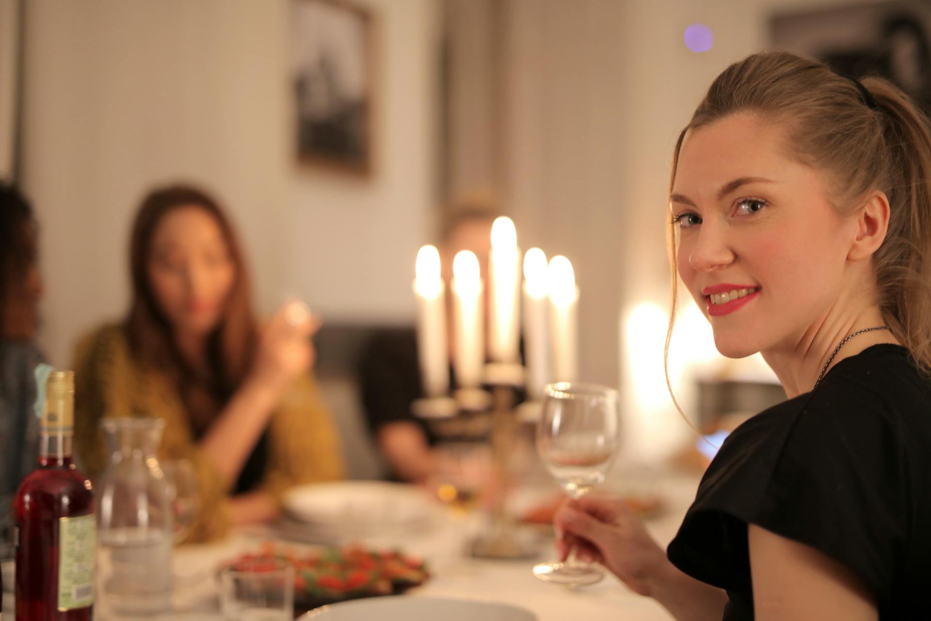 Une femme sourit en tenant un verre de vin à la table du dîner | Source : Pexels