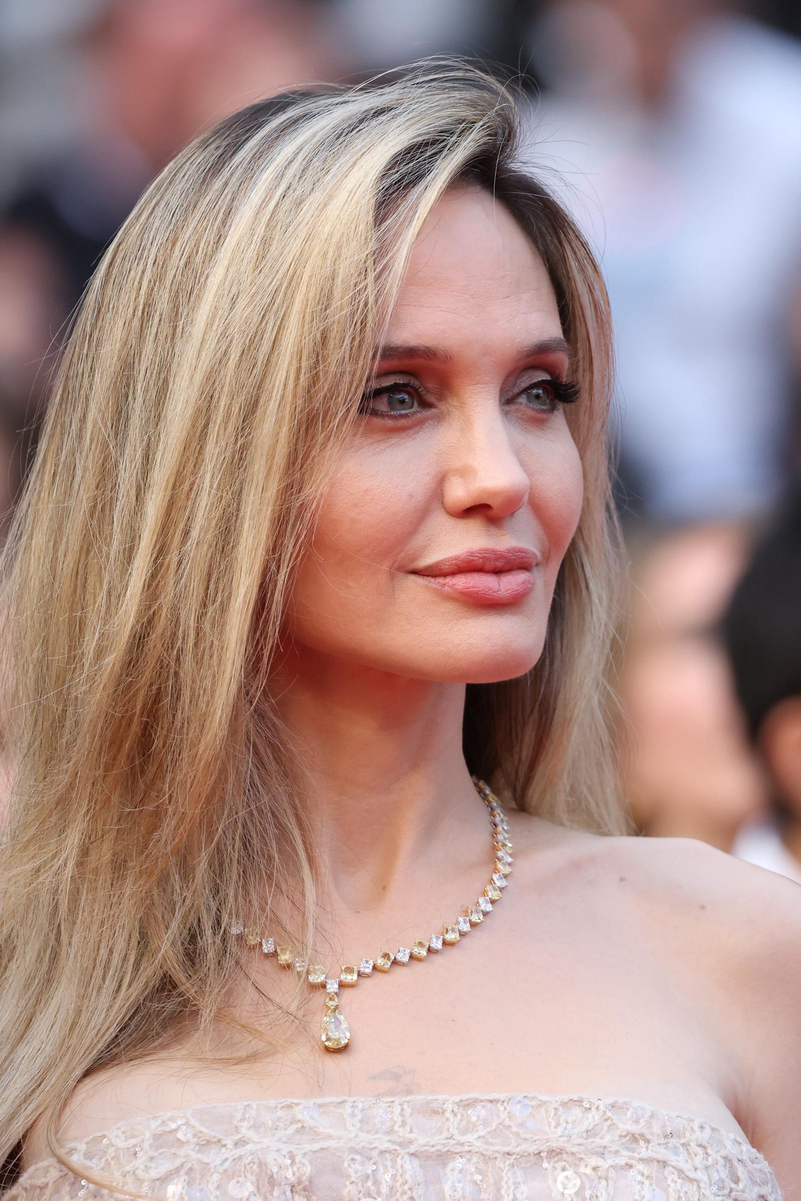 Dans un gros plan qui capture chaque détail poli, le maquillage soft glam et le collier de diamants d'Angelina Jolie brillent sous les lumières de Cannes, mettant en valeur son expression sereine et son élégance aux reflets dorés.