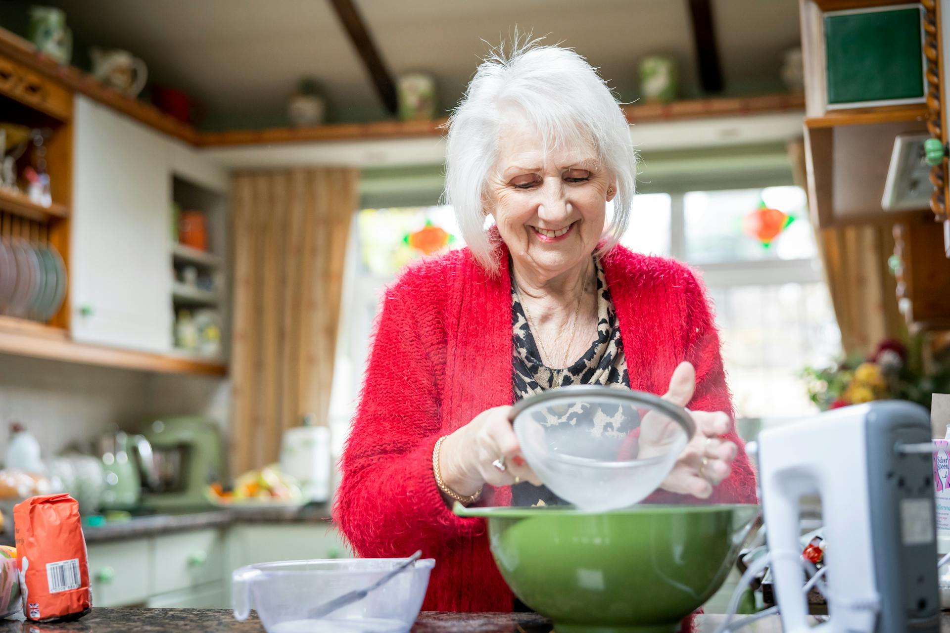 Une femme âgée souriante tamise de la farine dans sa cuisine | Source : Pexels