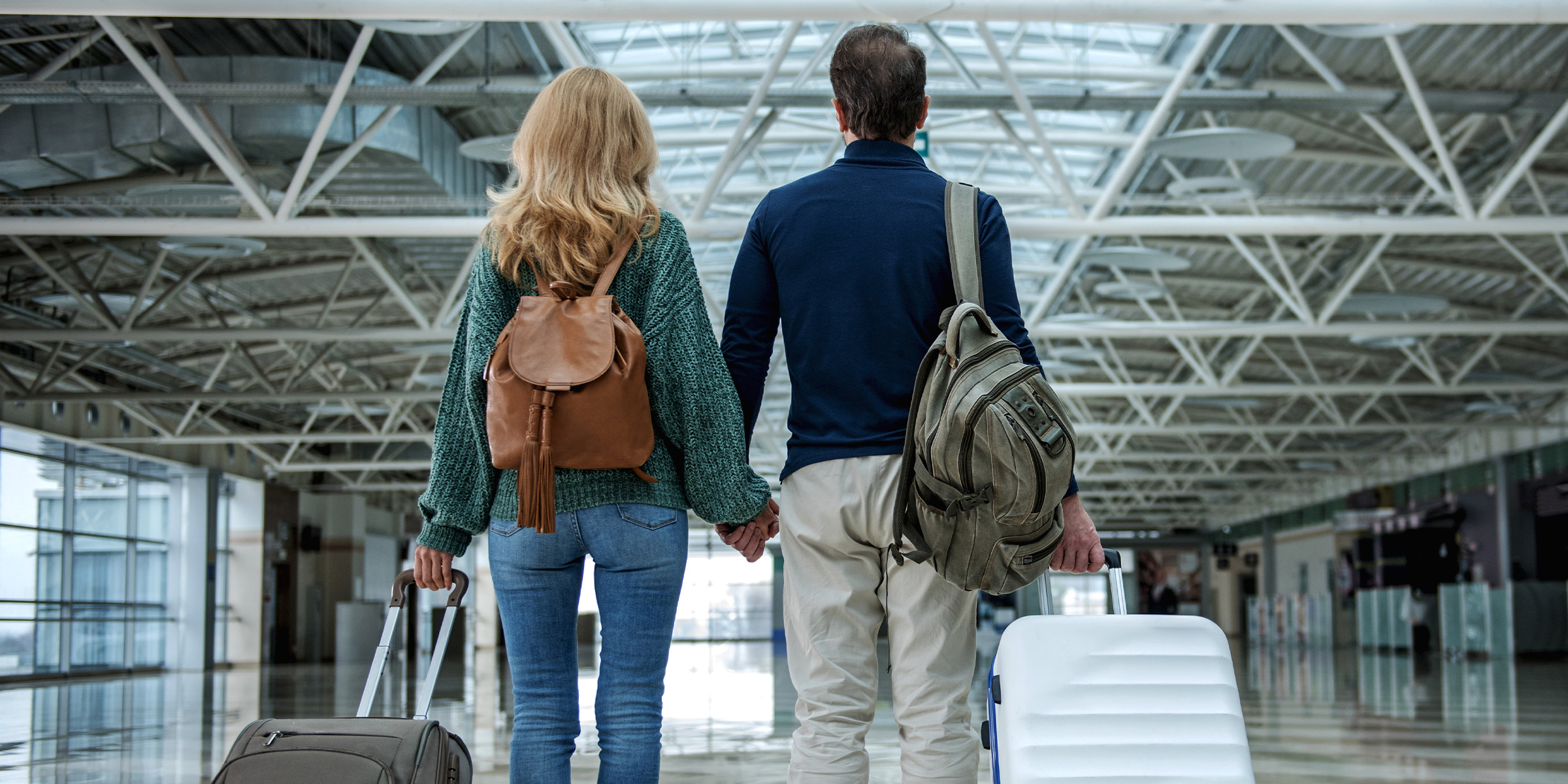 Un couple se tenant main dans la main dans un aéroport, chacun tenant une valise | Source : Shutterstock