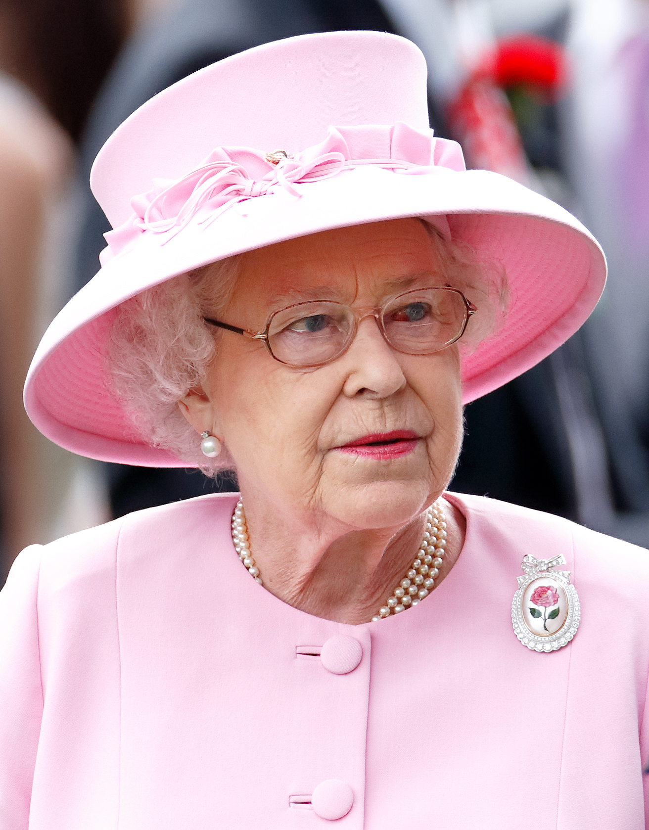 Lors de la deuxième journée du Royal Ascot, la reine Elizabeth II porte sa broche Centenary Rose, commandée spécialement pour l'occasion, ainsi qu'une tenue rose. La décoloration rouge de son œil gauche est visible lorsqu'elle interagit avec les participants.