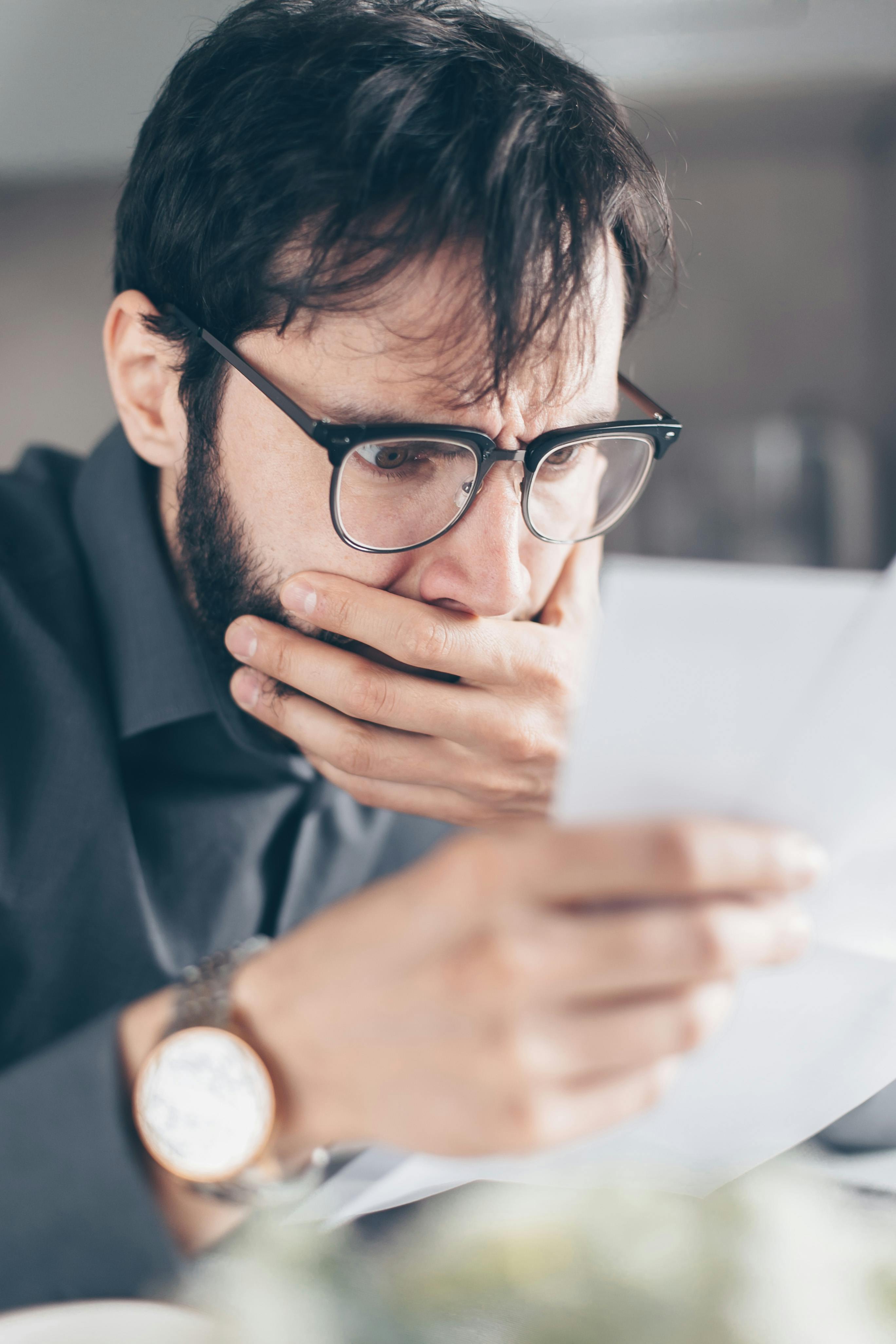 Un homme choqué se couvre la bouche tout en lisant quelque chose sur un papier | Source : Pexels