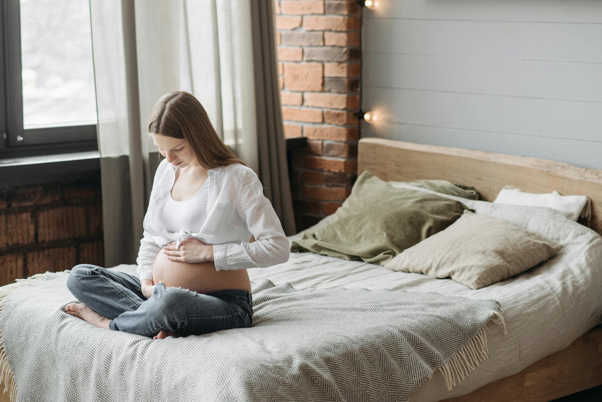 Une femme enceinte assise sur le lit se tenant le ventre | Source : Pexels