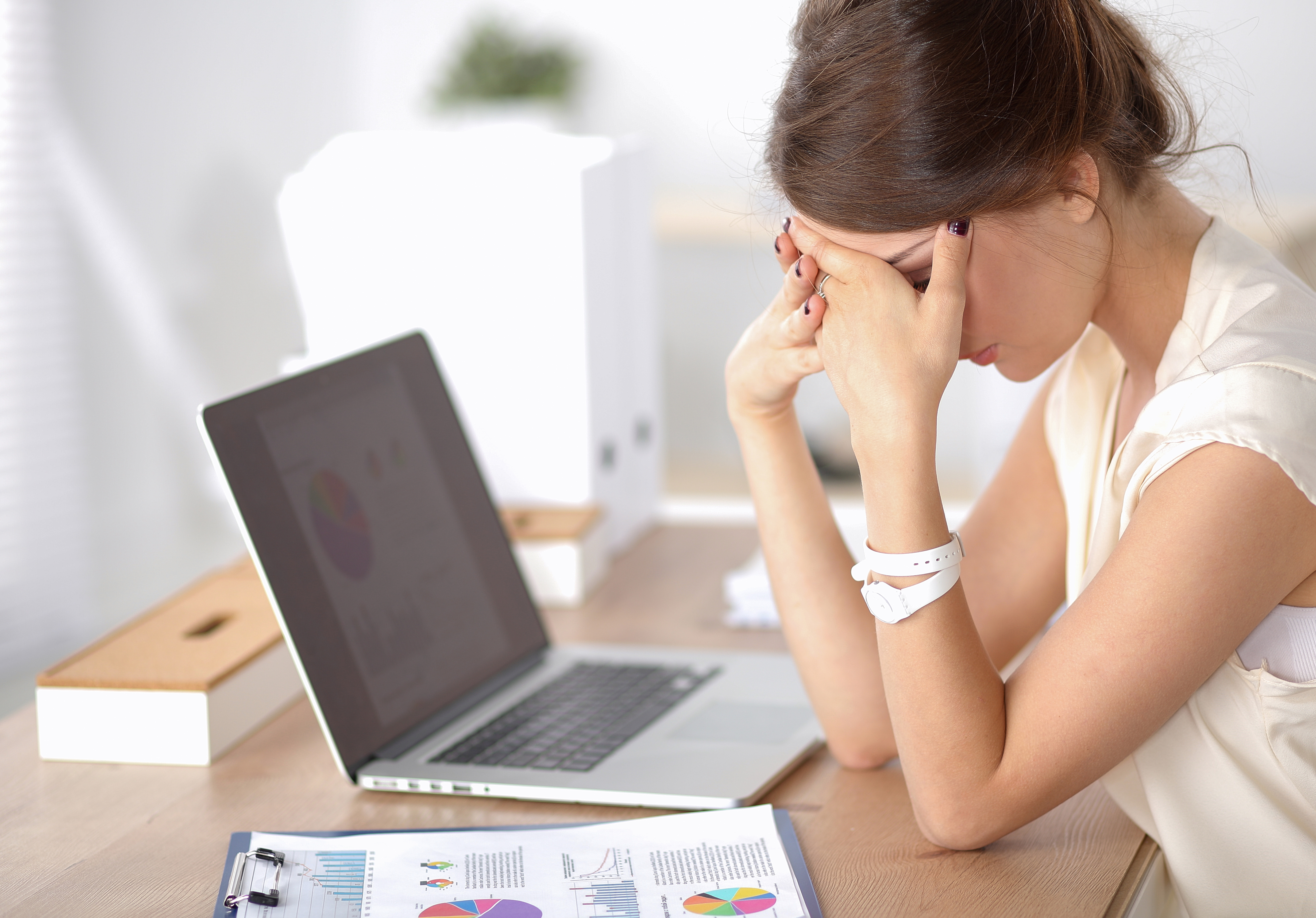 Uma mulher escondendo o rosto enquanto está sentado na frente de seu laptop | Fonte: Shutterstock