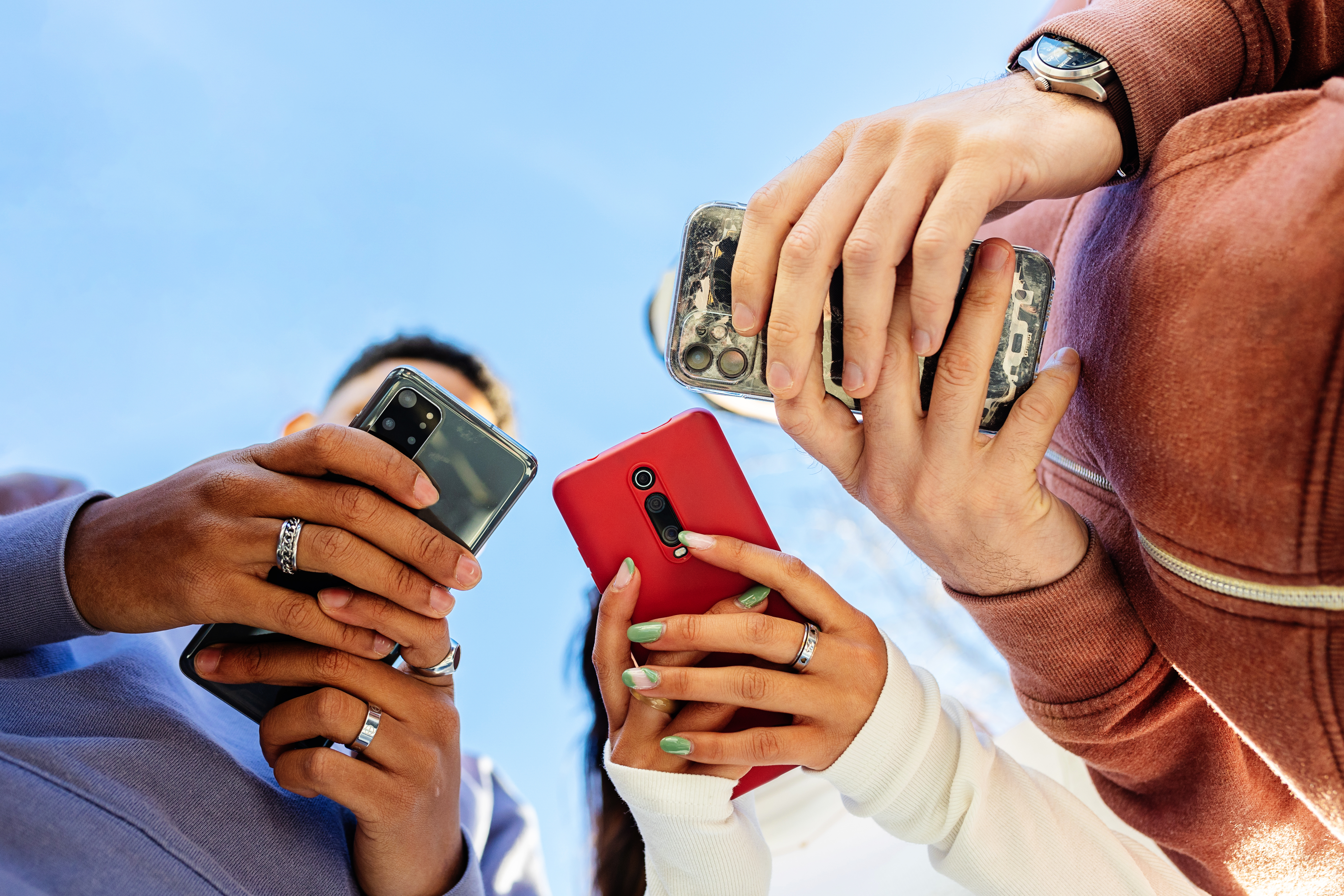 Vue en contre-plongée de trois jeunes gens utilisant leur téléphone portable à l'extérieur | Source : Getty Images