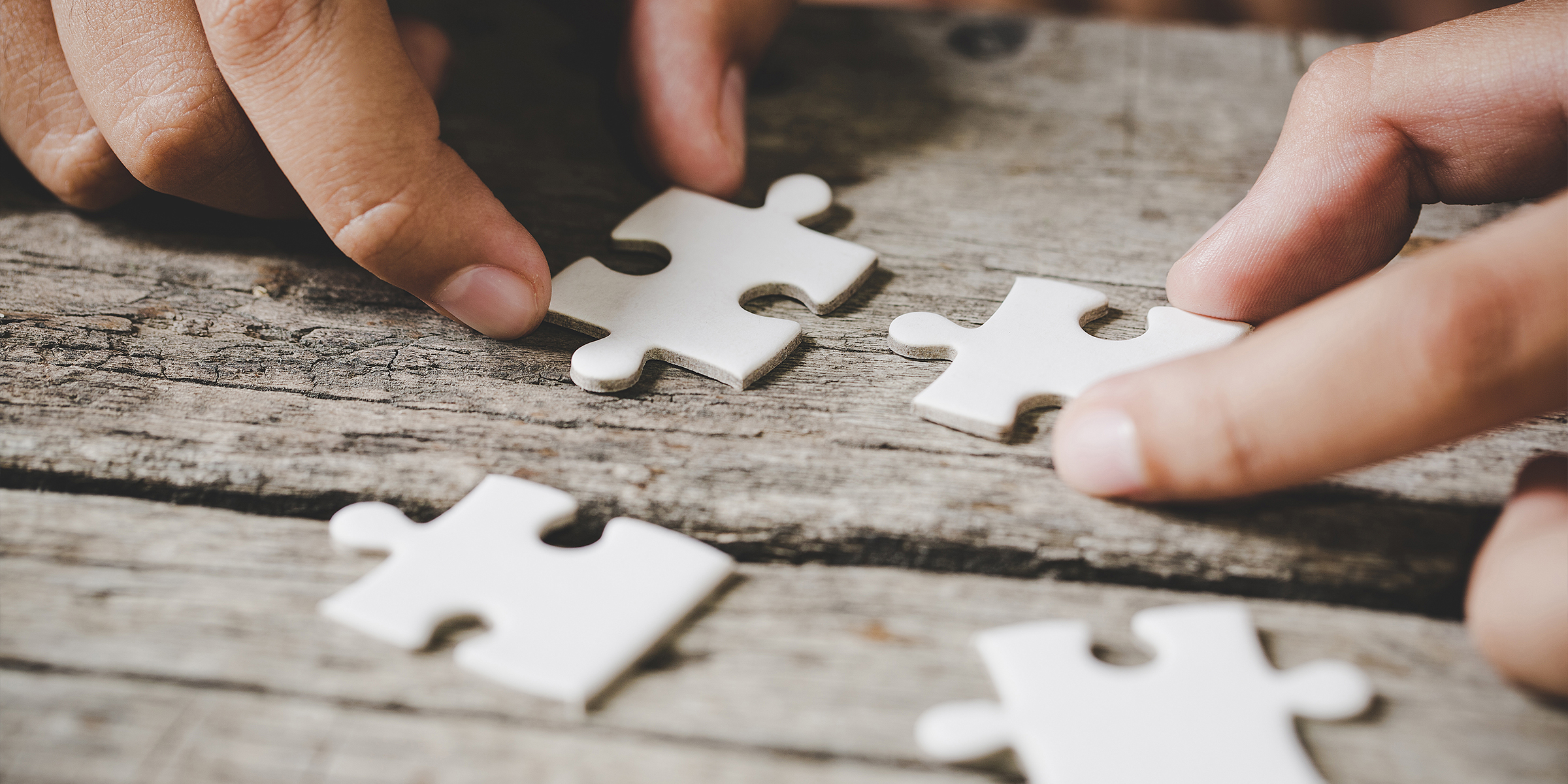 Une personne tenant les pièces d'un puzzle blanc sur une surface en bois | Source : Freepik