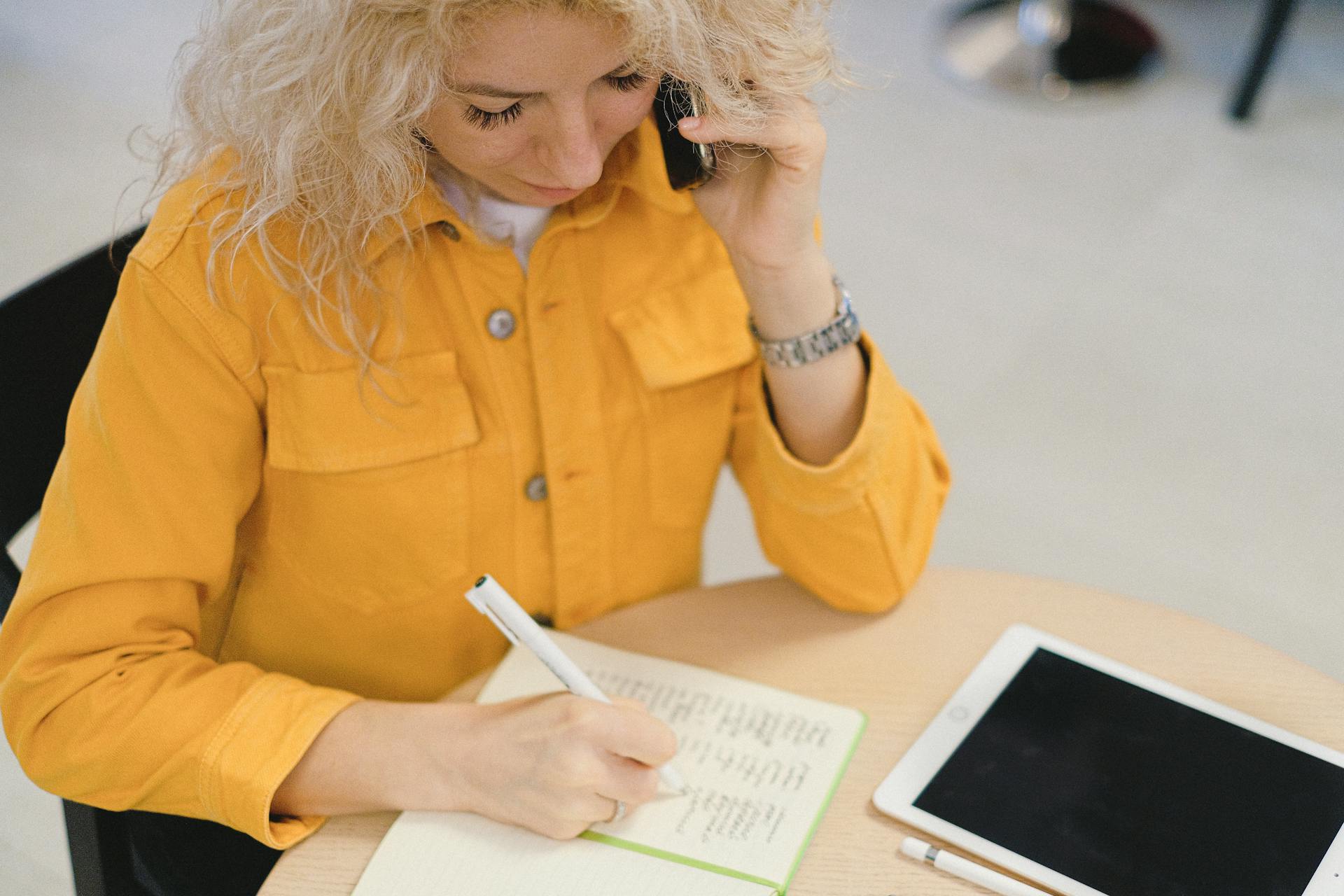 Une femme écrit dans son carnet tout en assistant à un appel | Source : Pexels